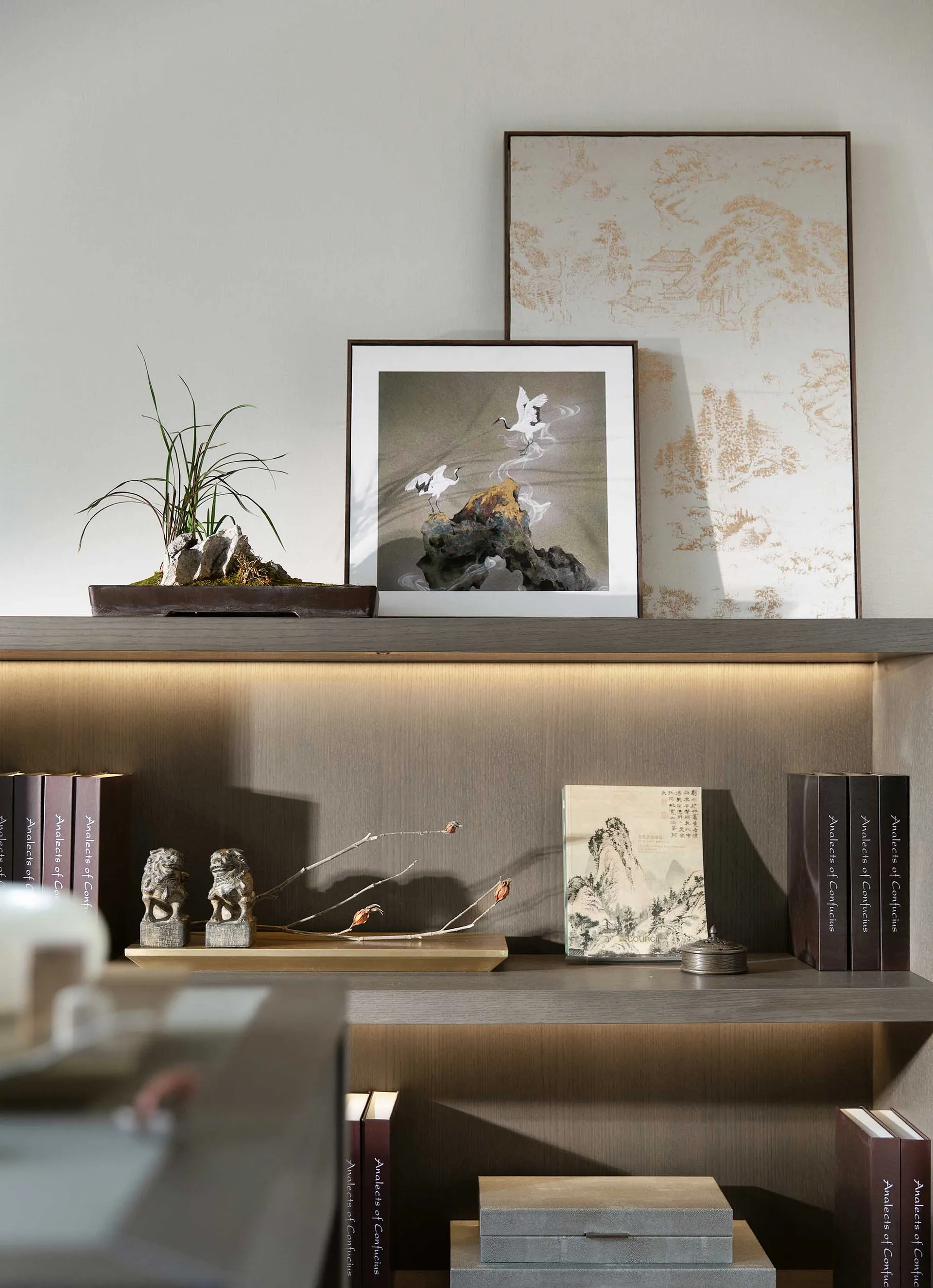 A modern shelf decorated with wooden elements, including books, a bonsai plant, and framed art.