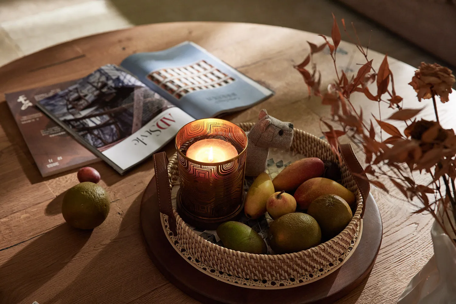 A cozy coffee table setting with a brass candle holder, wooden tray, leather details, and a variety of fresh fruits and dried