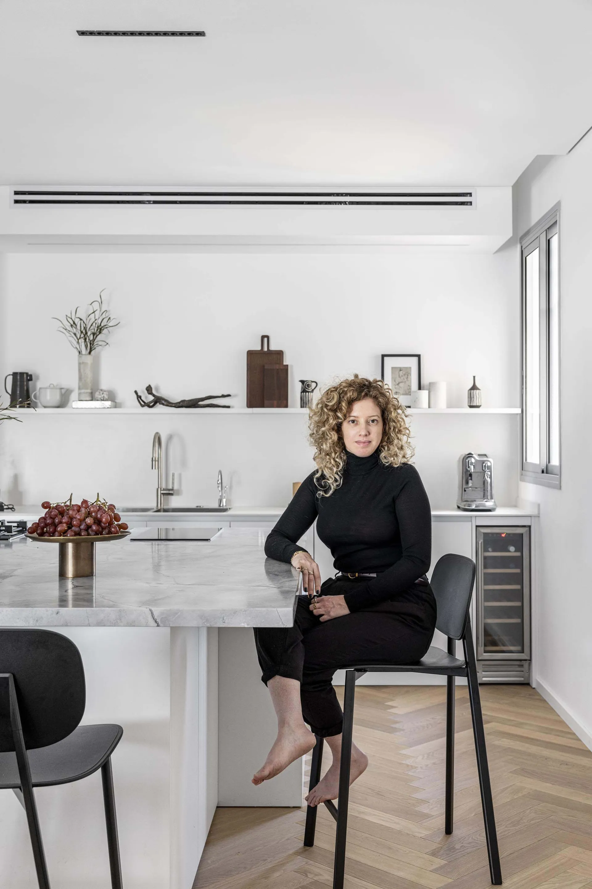 A minimalist kitchen featuring a marble countertop with a woman sitting on a stool.