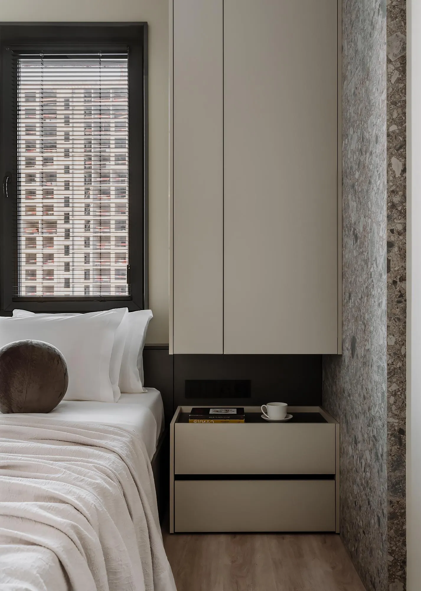 Minimalist bedroom featuring a bed with white bedding and a modern nightstand with a cup and books, set against a terrazzo wa
