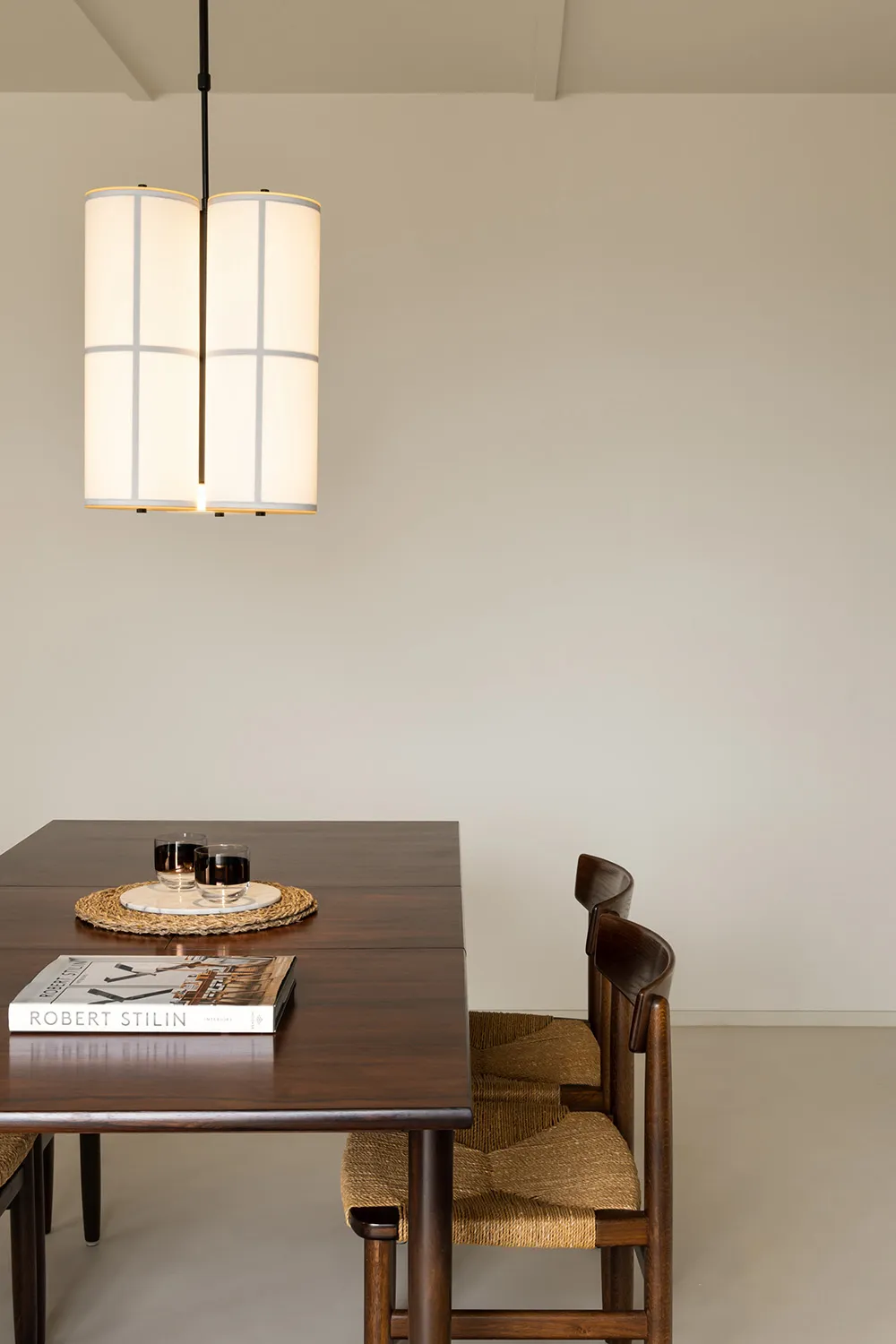 Minimalist dining room with wooden furniture, a wooden dining table with a glass vase and a book, and wooden chairs with wove