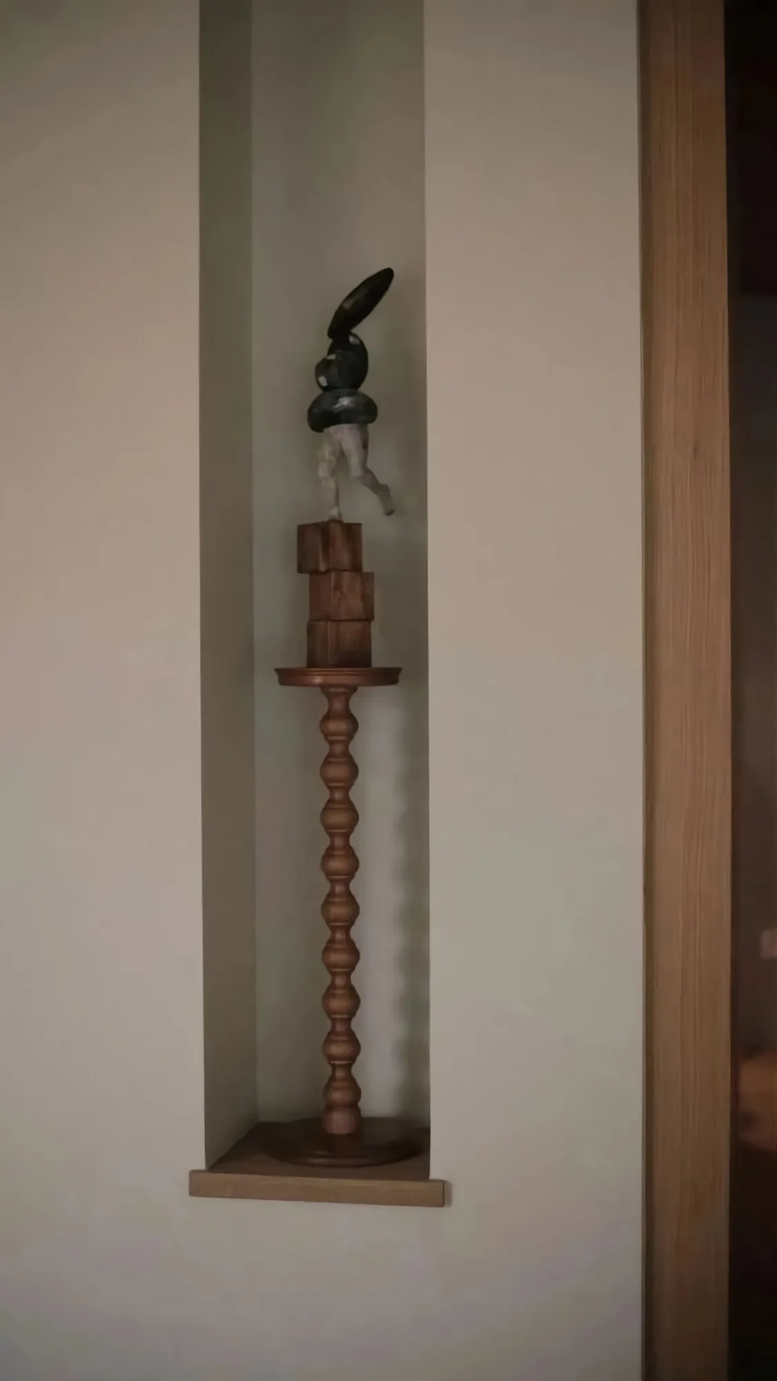 A modern interior design featuring a wooden pedestal with a sculpture displayed on top.