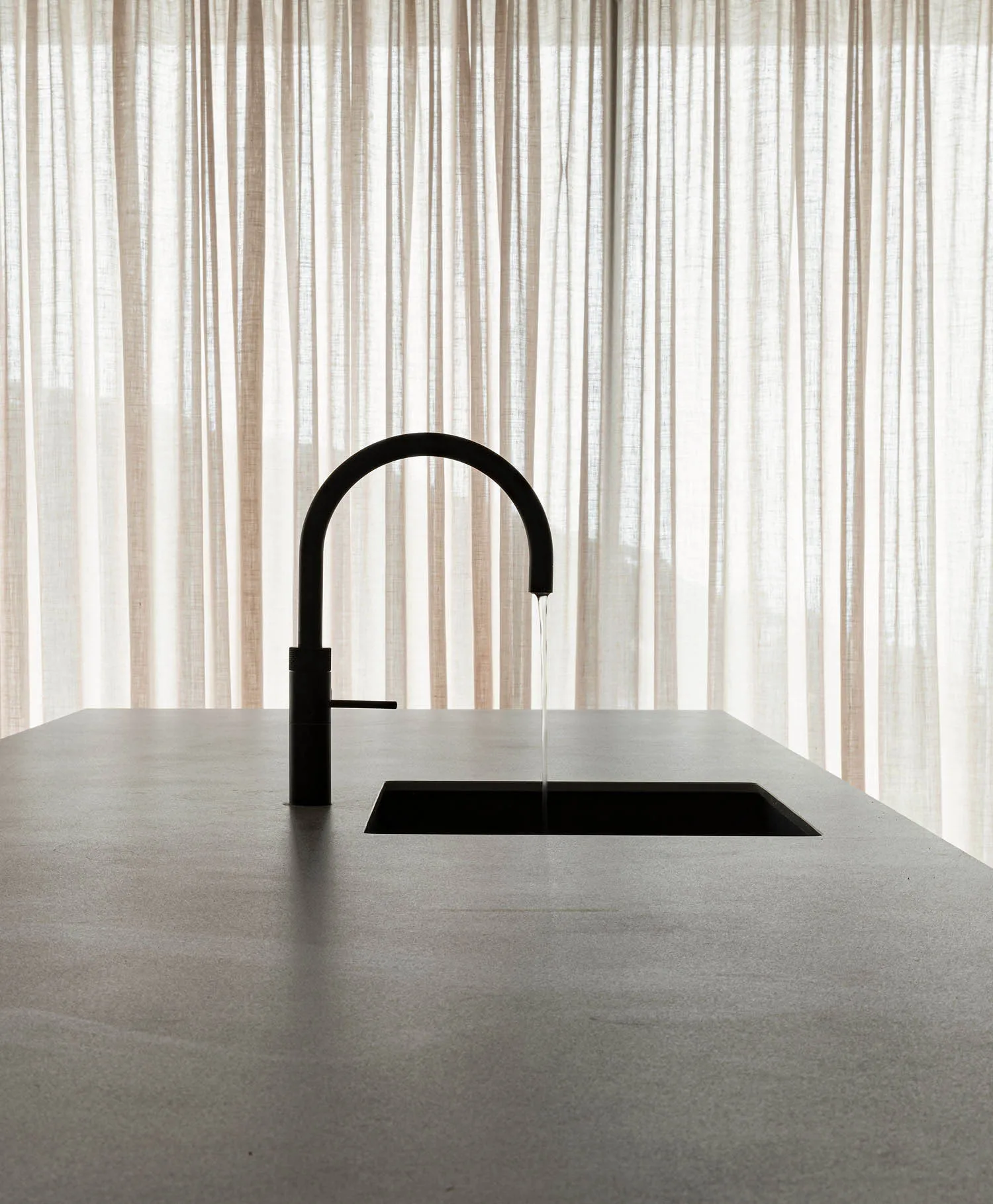 A minimalist modern kitchen featuring a concrete countertop and sink with a black faucet.