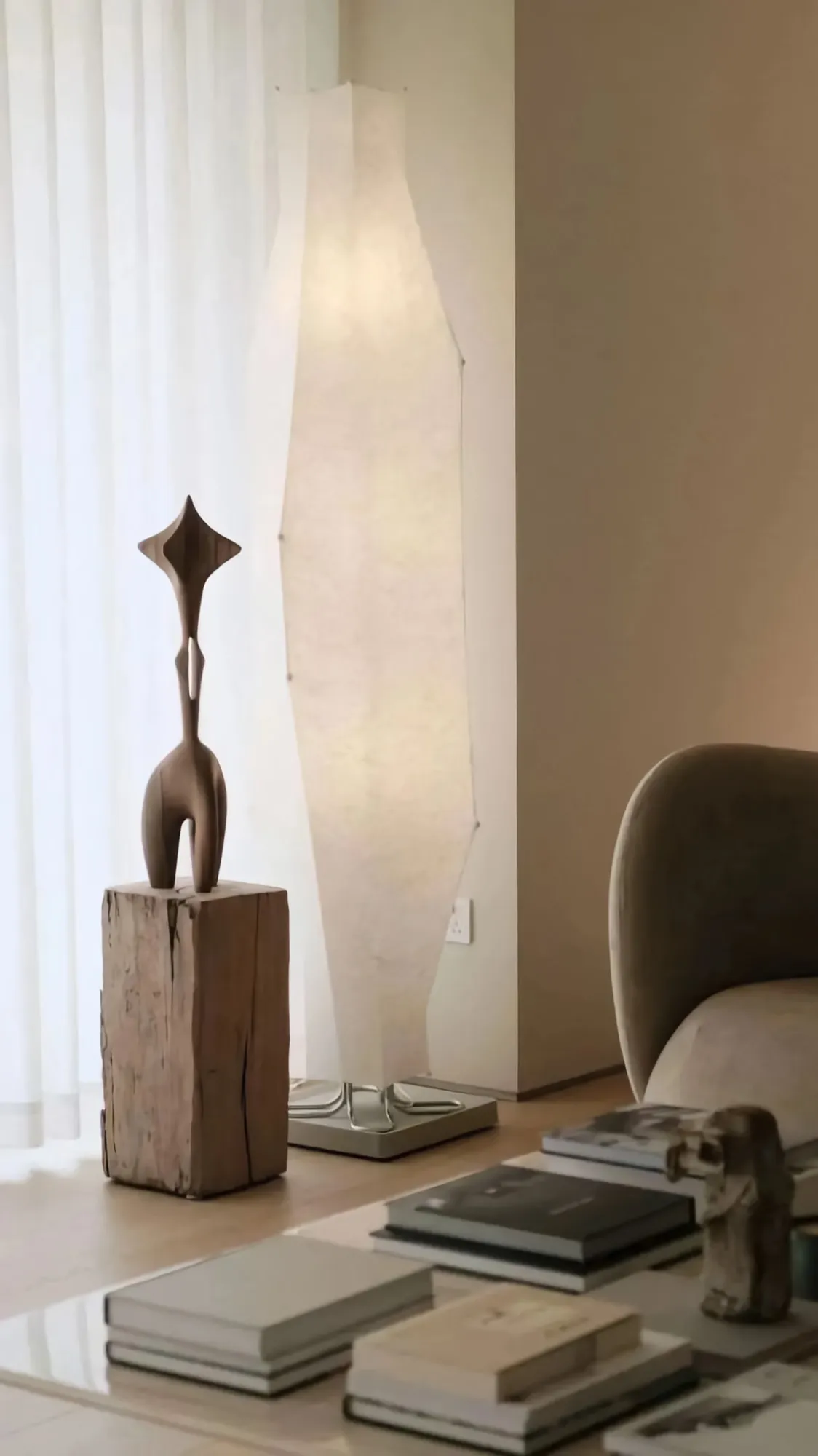 A modern living room with a wooden sculpture on a wooden pedestal, soft lighting, and minimalist decor.