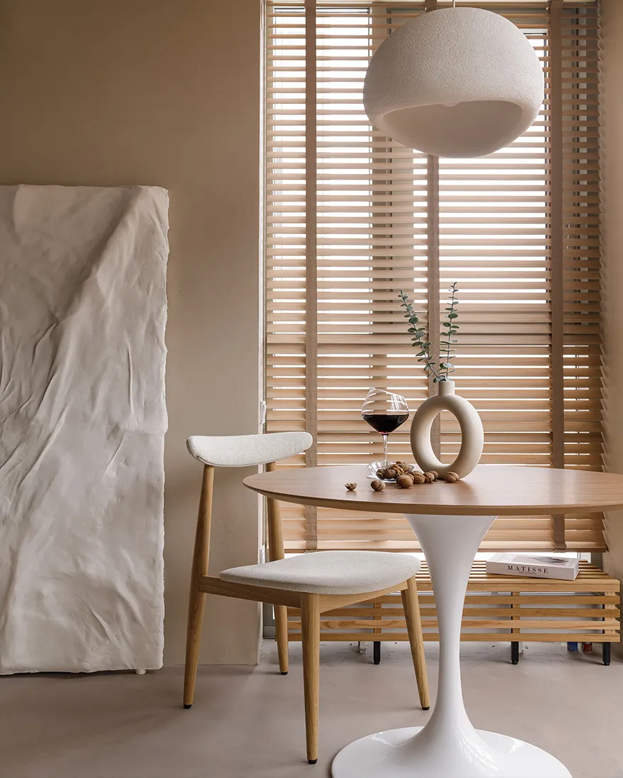 Contemporary dining area featuring a minimalist design with white fabric upholstery and wooden elements, including a round ta