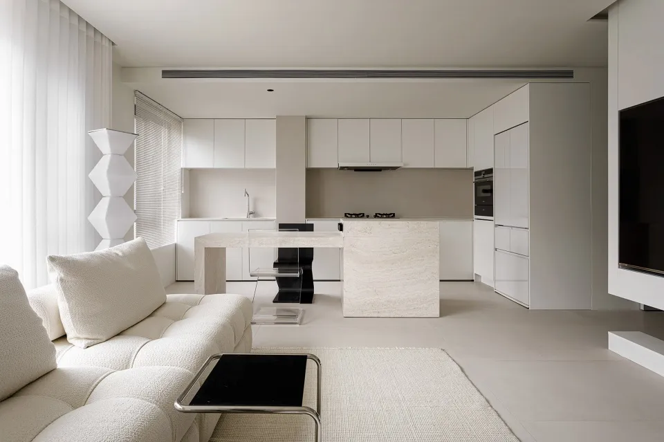 A modern minimalist kitchen with white cabinets, a marble kitchen island, and a white sofa in the foreground.