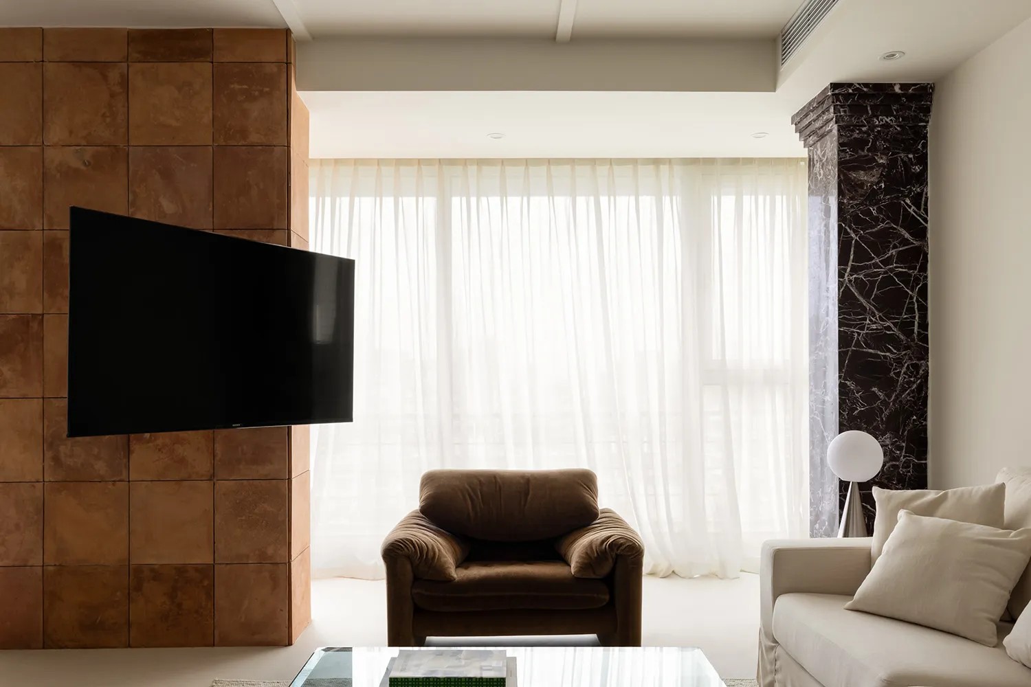 A modern minimalist living room featuring a black flat-screen TV on a terracotta tiled backdrop, a white sofa adorned with be