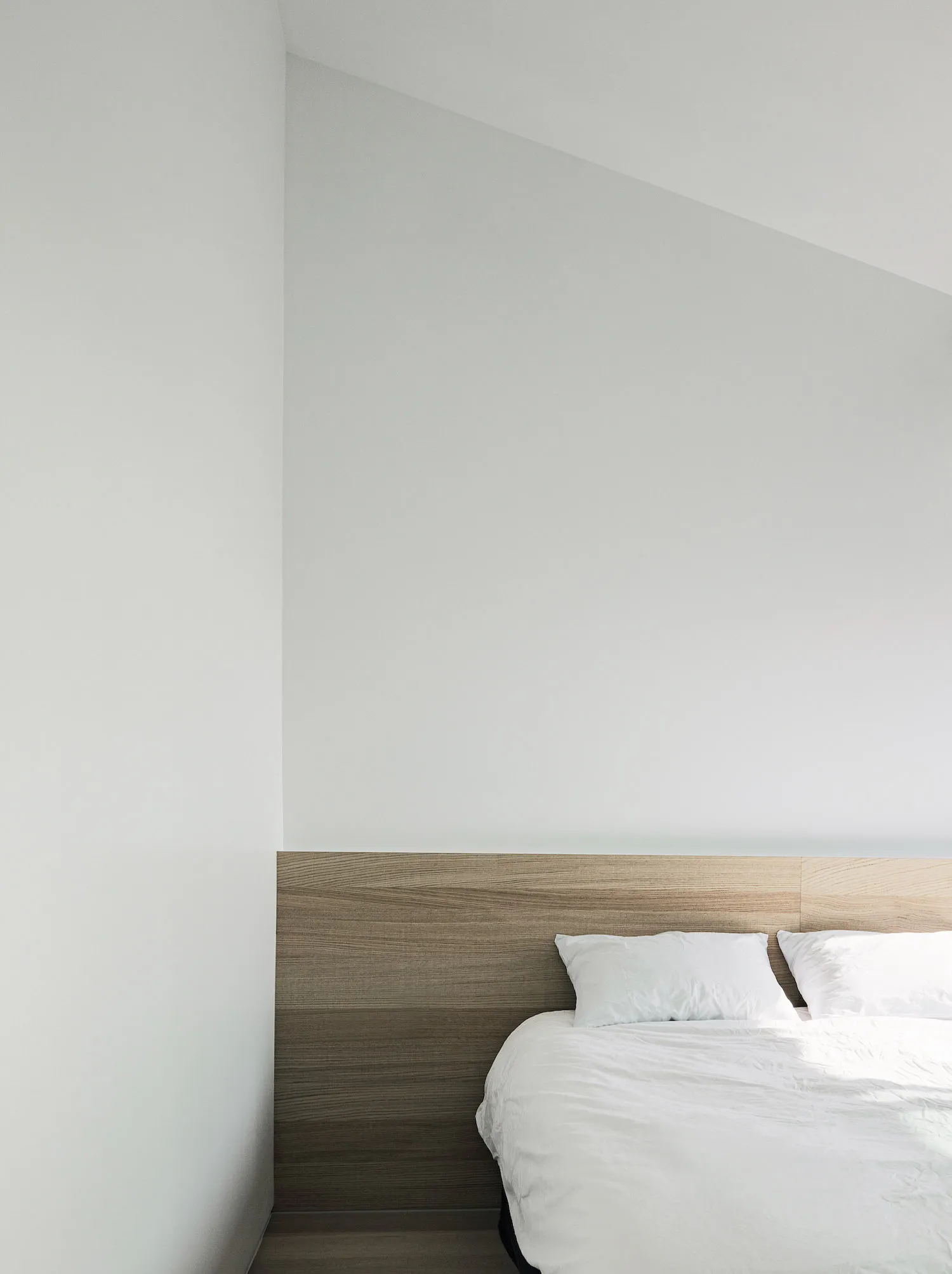 A minimalist bedroom featuring wooden accents and a white bed.