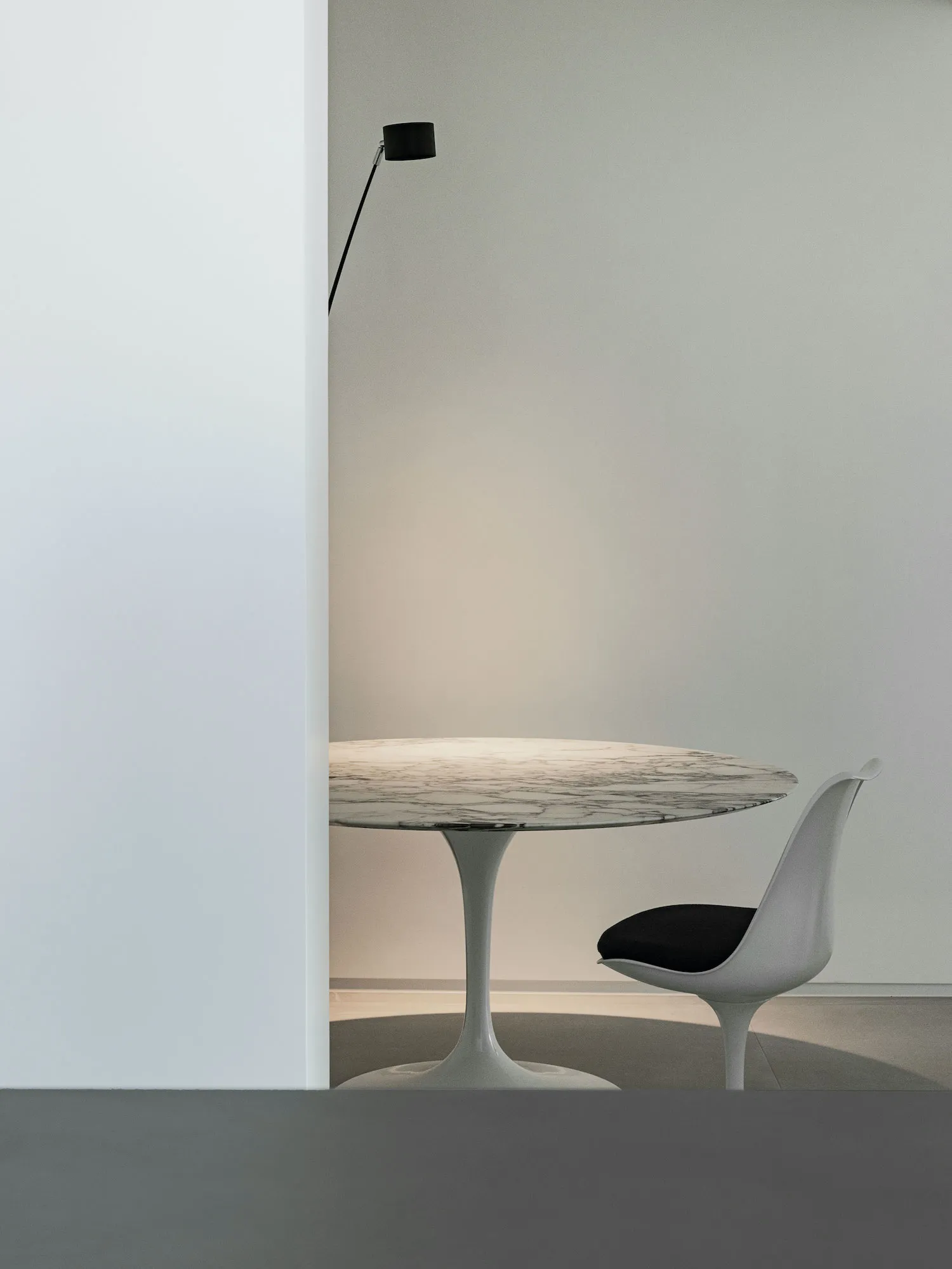 A minimalist modern dining room featuring a round marble table with a sleek, white tulip base and a single white chair with a