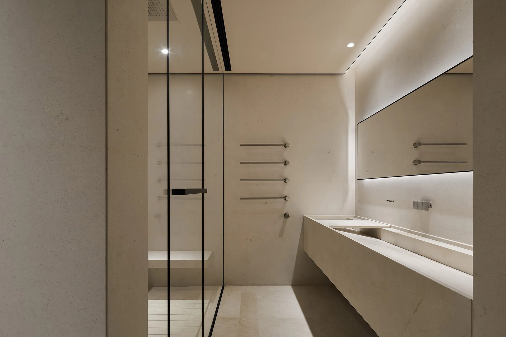 Modern minimalist bathroom with concrete walls and floor, featuring a sleek white sink and illuminated mirror.
