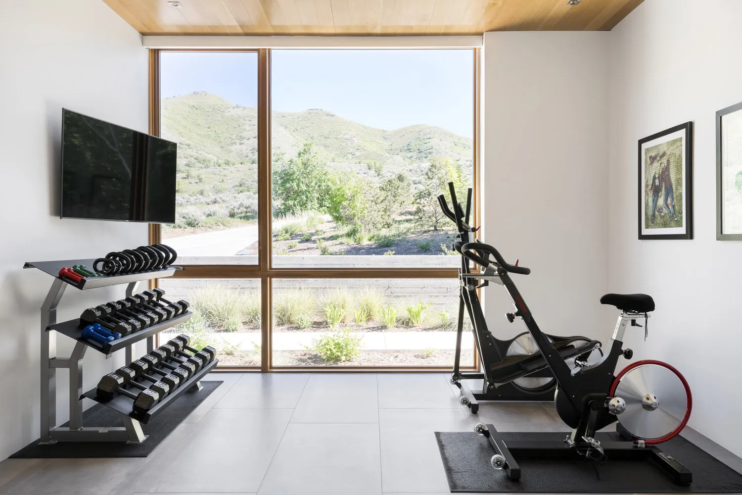 A minimalist home gym featuring a black stationary bike and a dumbbell rack against a white wall with a large window showcasi
