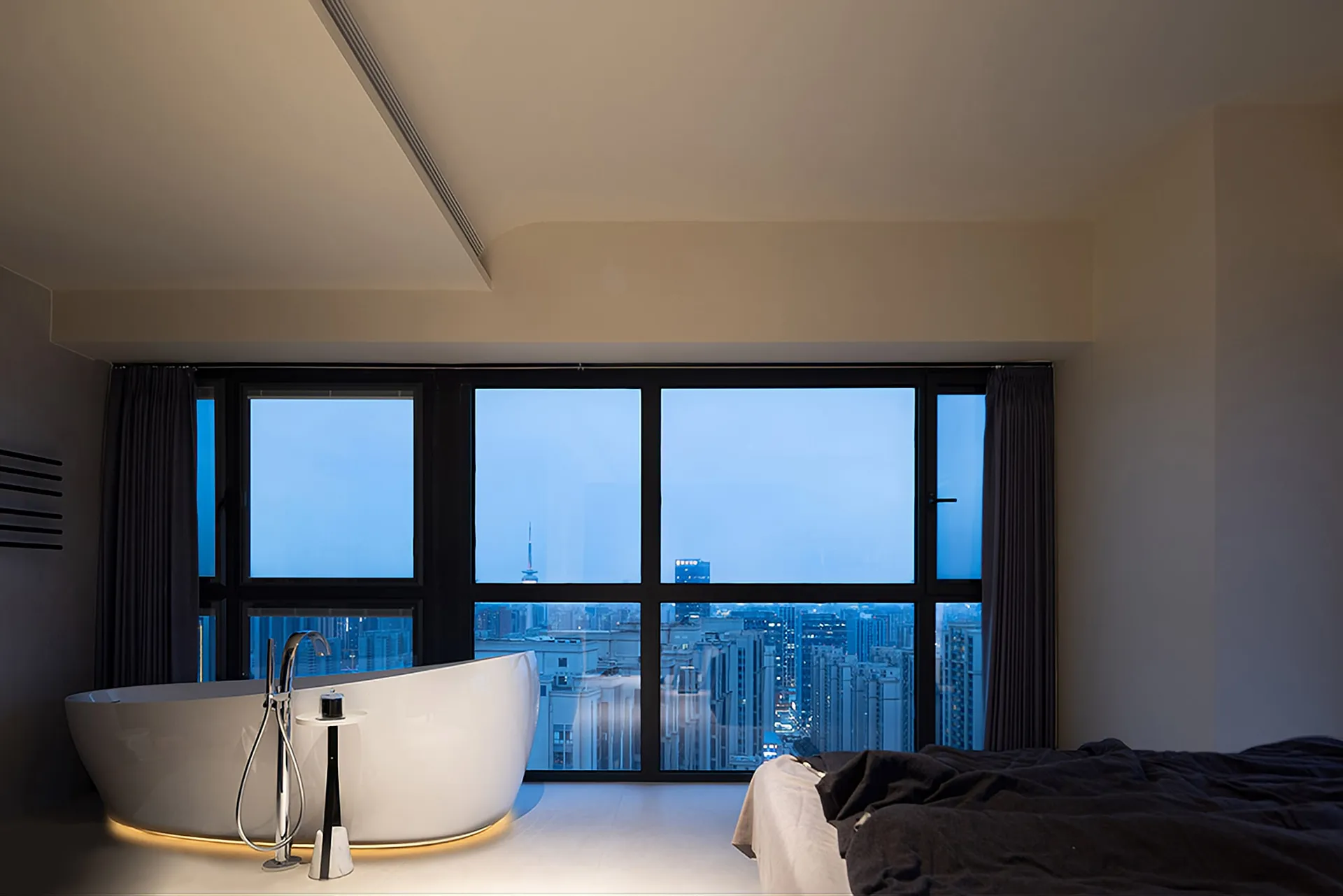 Modern bathroom featuring a large free-standing bathtub with a cityscape view through the floor-to-ceiling windows.