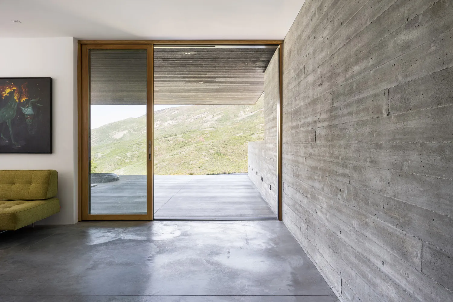 A modern interior space featuring a concrete wall and large sliding glass door looking out to a mountain landscape.