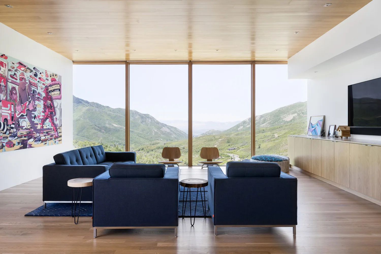 Modern living room featuring blue furniture, large windows with a mountain view, and a wooden floor.