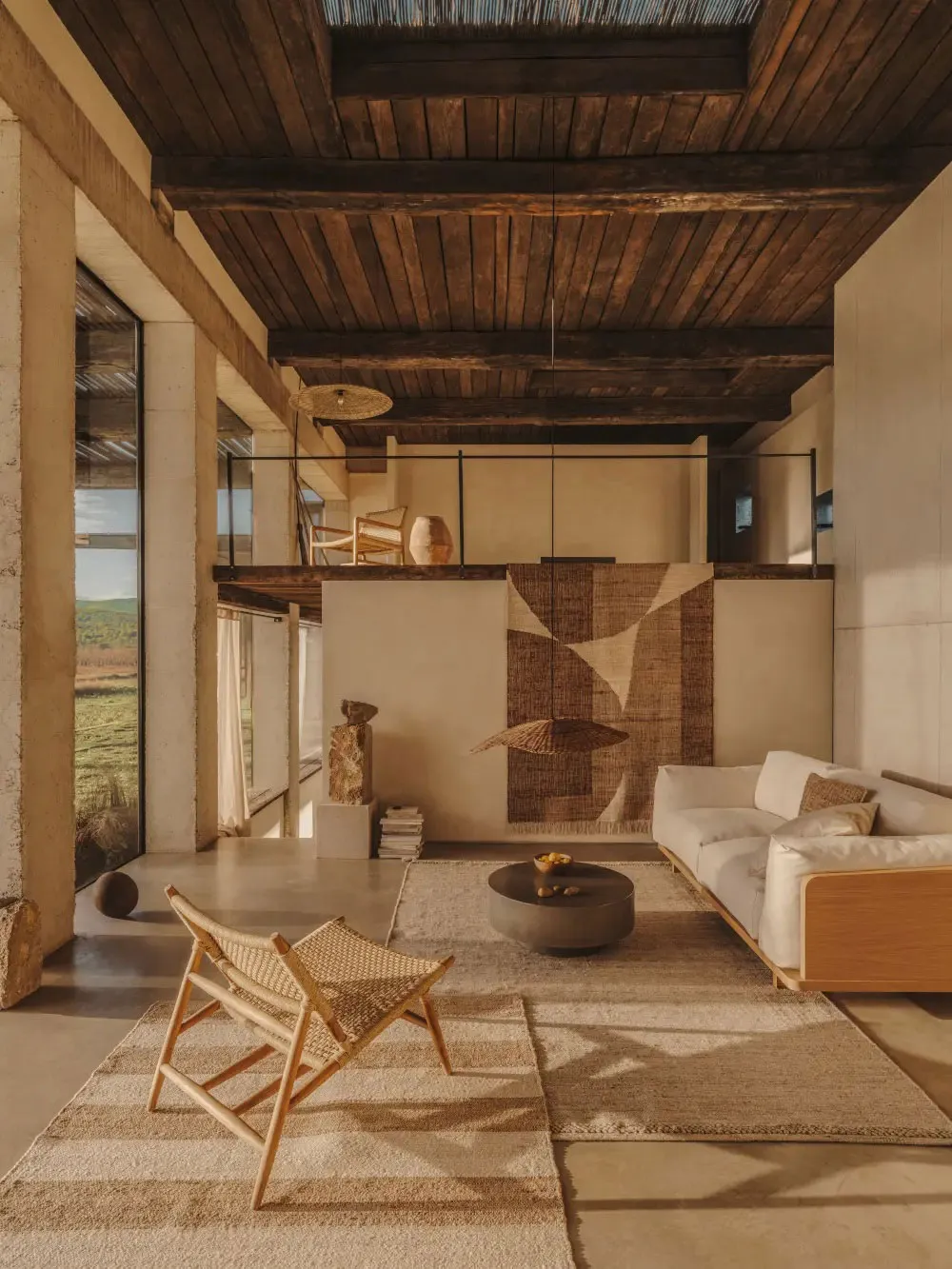 Modern living room featuring a concrete floor, wooden ceiling beams, and a textured rug, with a white sofa and woven armchair