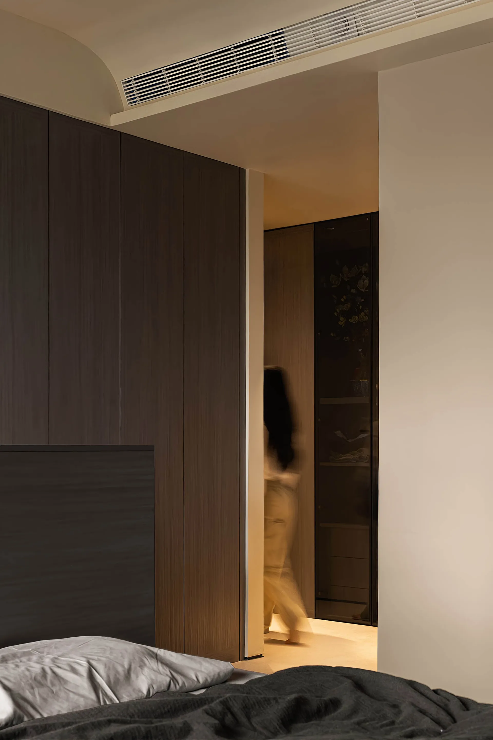 A modern minimalist bedroom featuring dark wood cabinets and warm lighting.