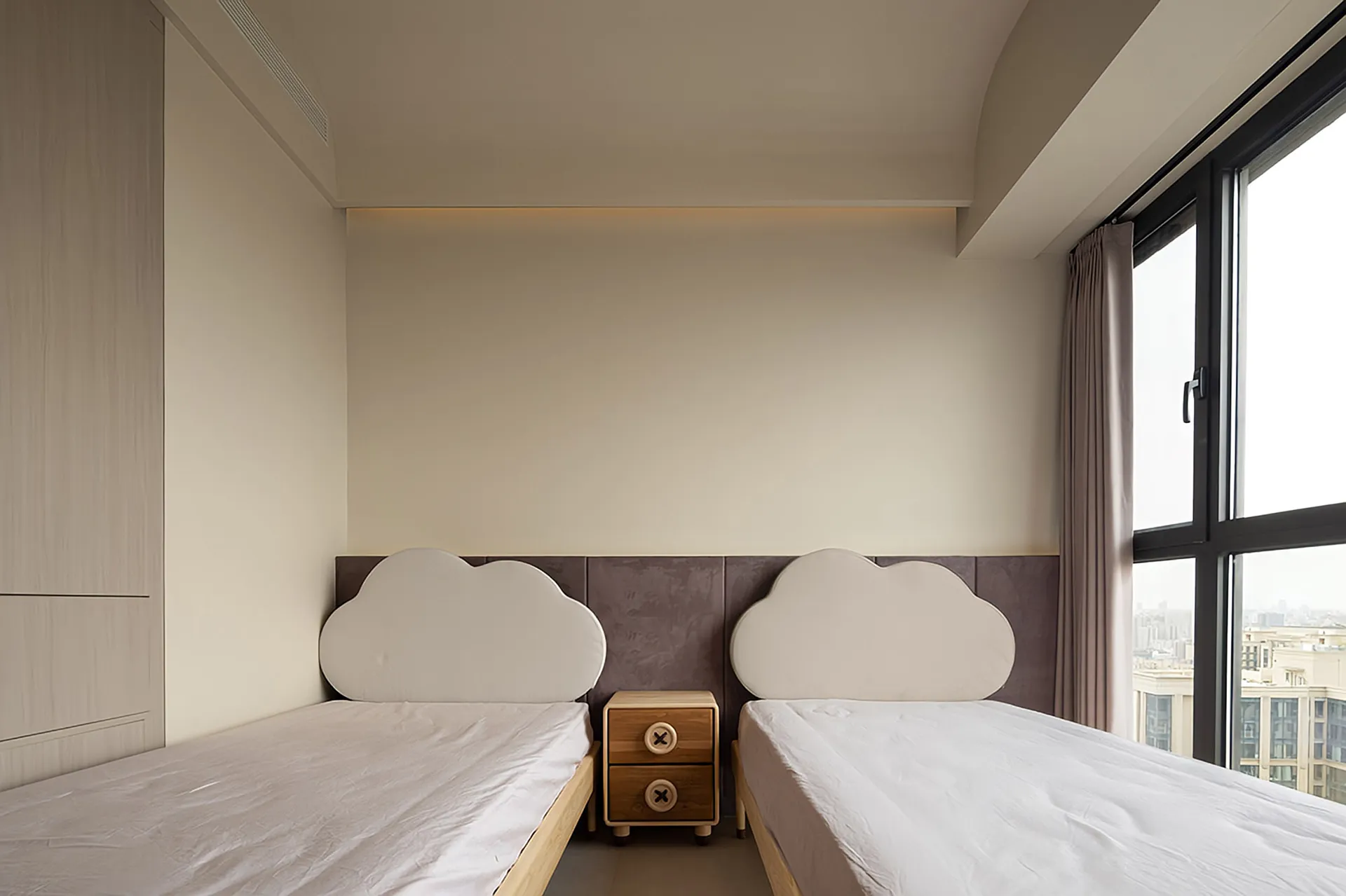 A minimalist bedroom with a cloud-shaped upholstered headboard, white bedding, and a small wooden nightstand between two sing