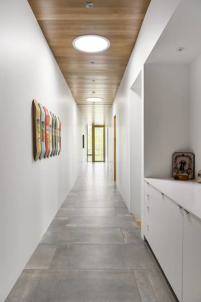 A modern corridor with a concrete floor, white walls, and wooden ceiling.