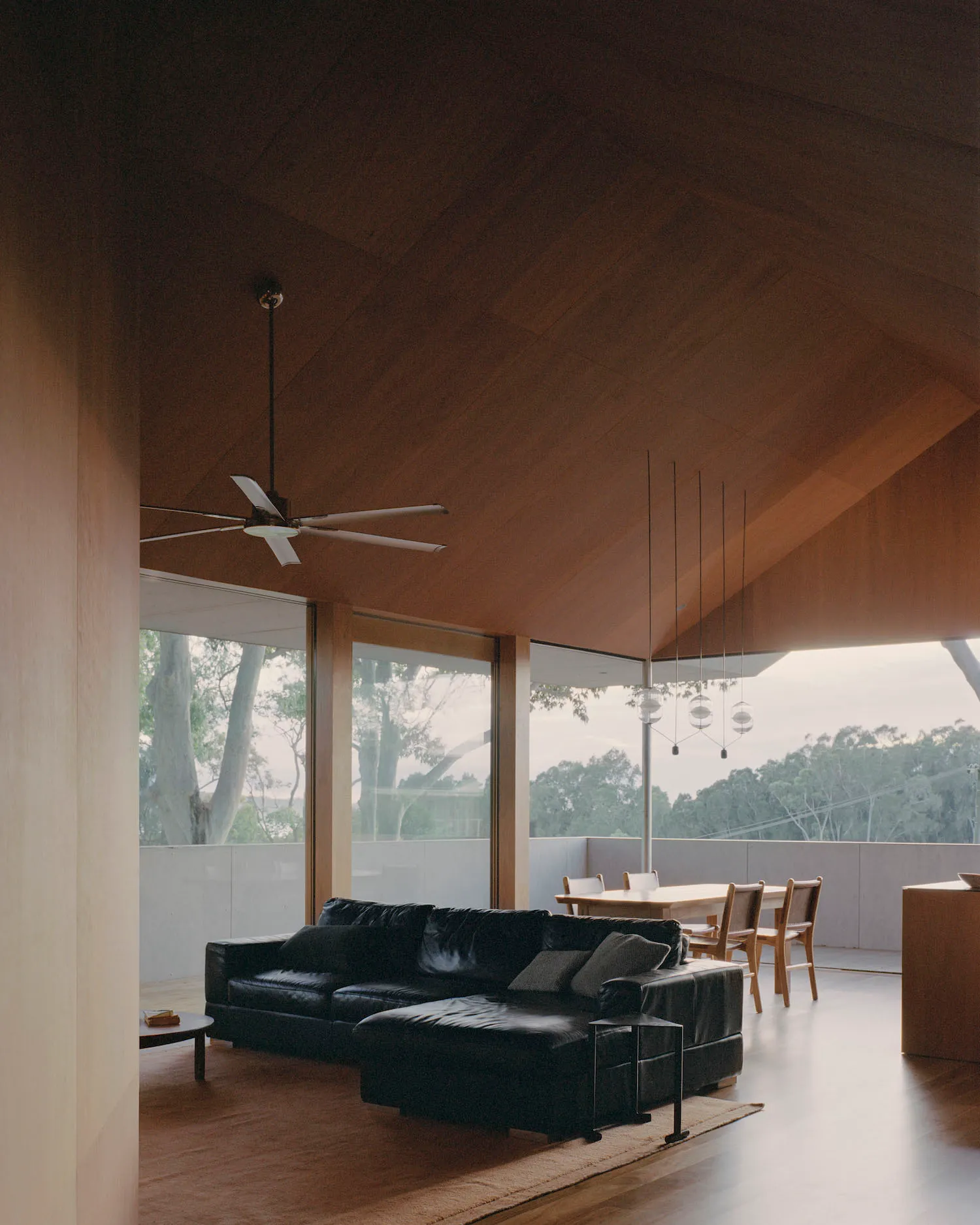 A modern living room featuring wooden walls, a black leather sectional sofa, and a glass table with chairs.