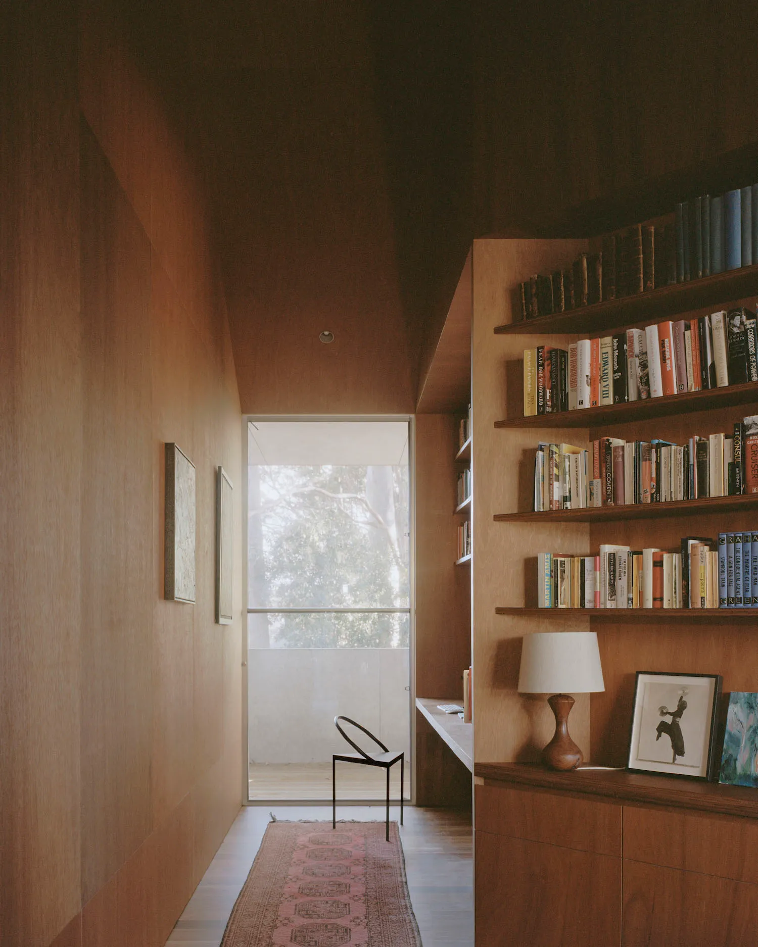 A minimalist home library featuring a wooden wall and shelves filled with books.