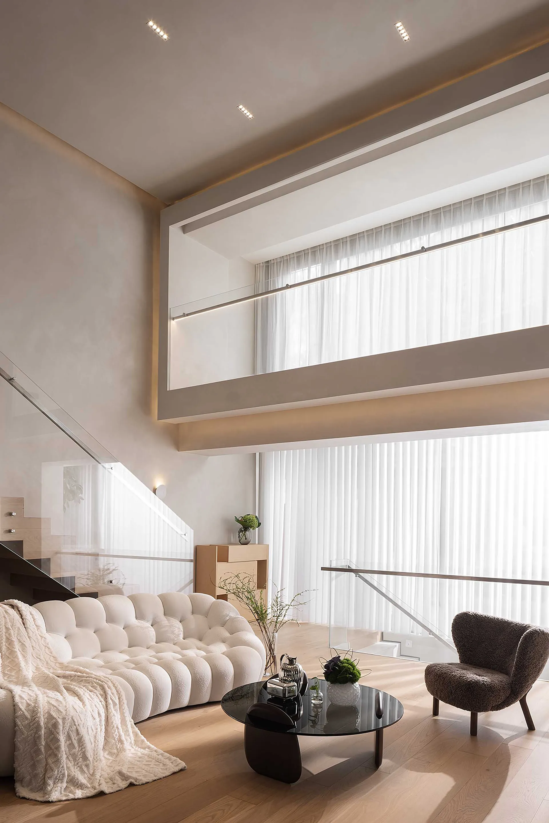 A modern living room featuring a white sofa and wooden floors, with large windows allowing natural light to flood the space.