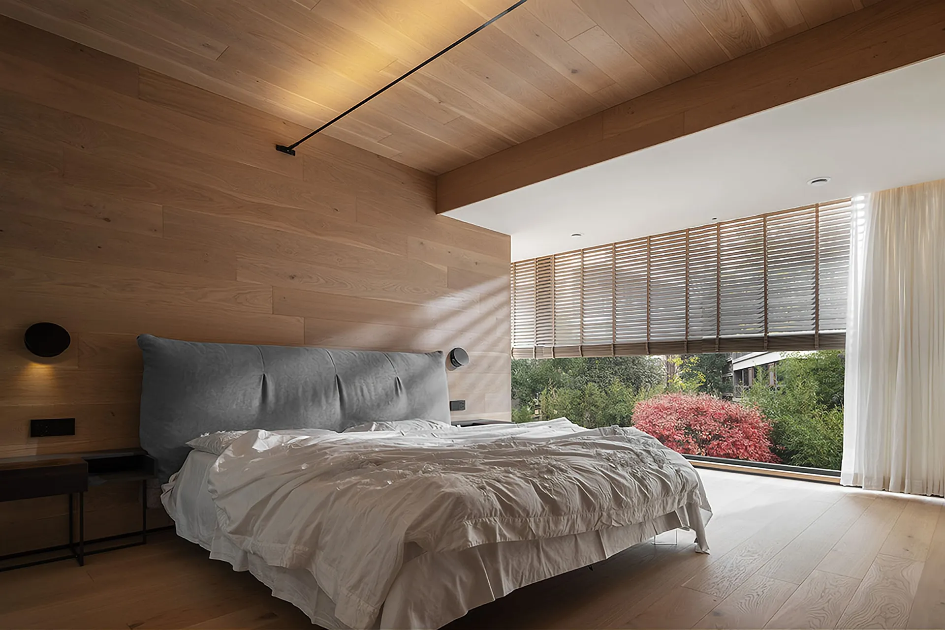 Modern bedroom with wooden walls, ceiling, and floor, featuring a comfortable bed with a grey cushioned headboard and neutral