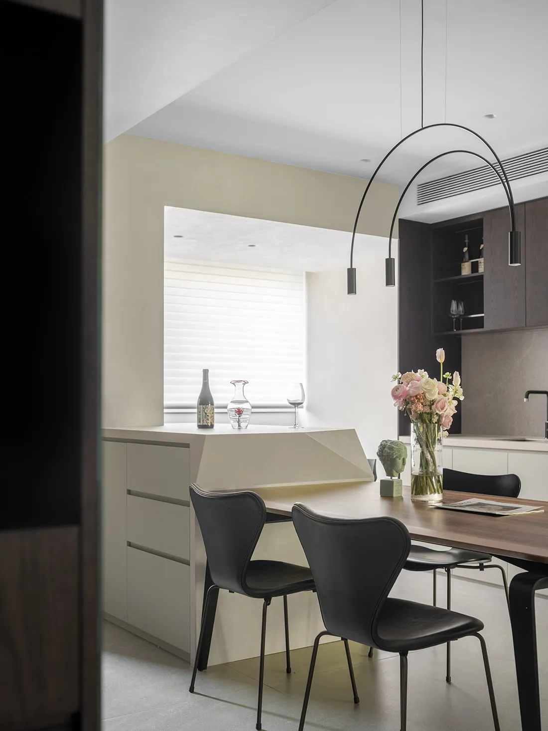 Modern kitchen with wooden table, black chairs, and a vase of flowers.