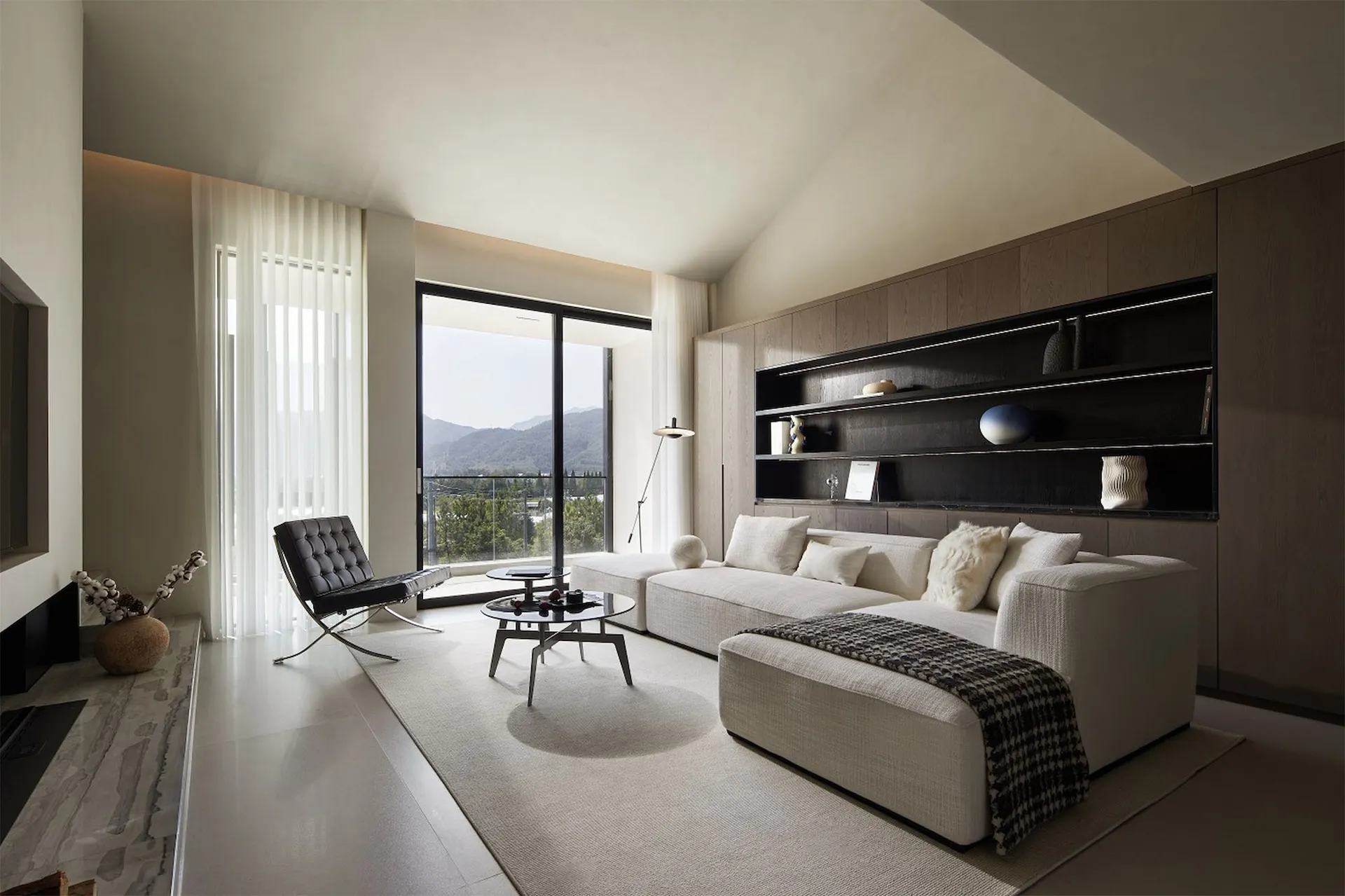 A modern living room featuring white furniture and minimalist decor, with large windows providing natural light and scenic vi