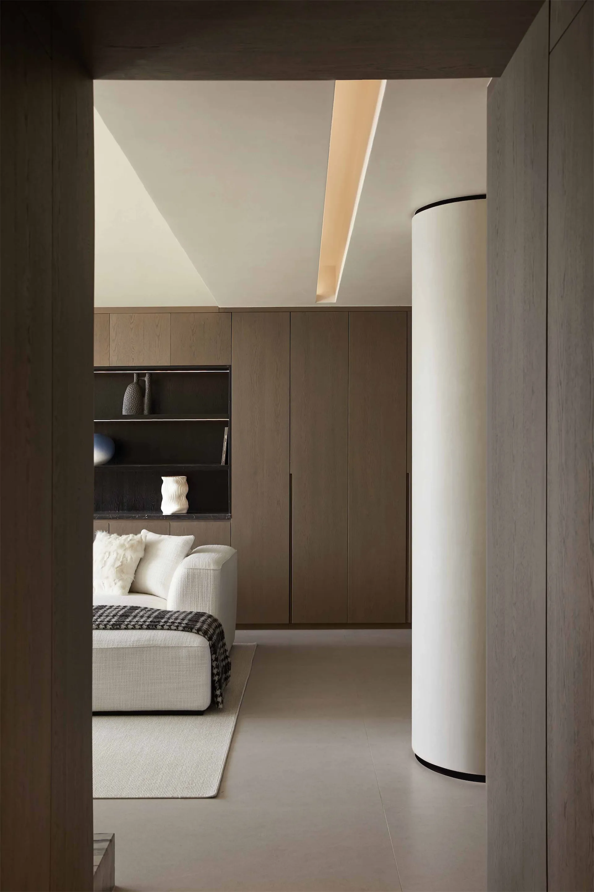 Modern minimalist living room with a white sofa, wooden cabinets, and a sleek light fixture.