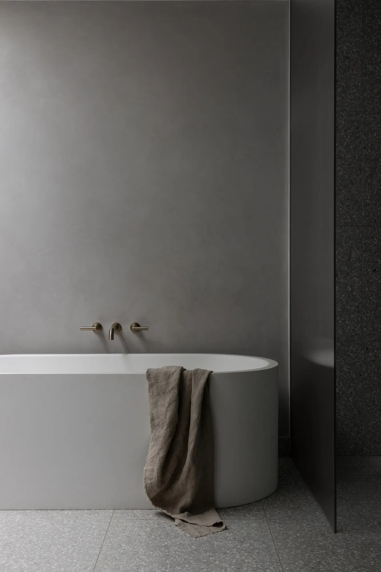 A minimalist bathroom with a freestanding concrete bathtub and a towel draped over the edge.