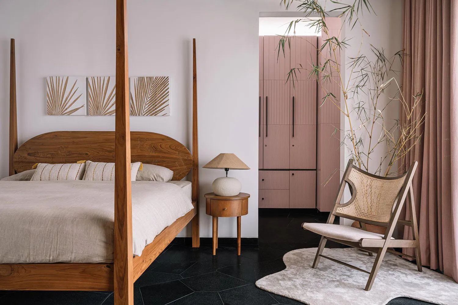 A modern bedroom featuring a wooden four-poster bed, a side table with a lamp, and a chair with a wicker backrest.