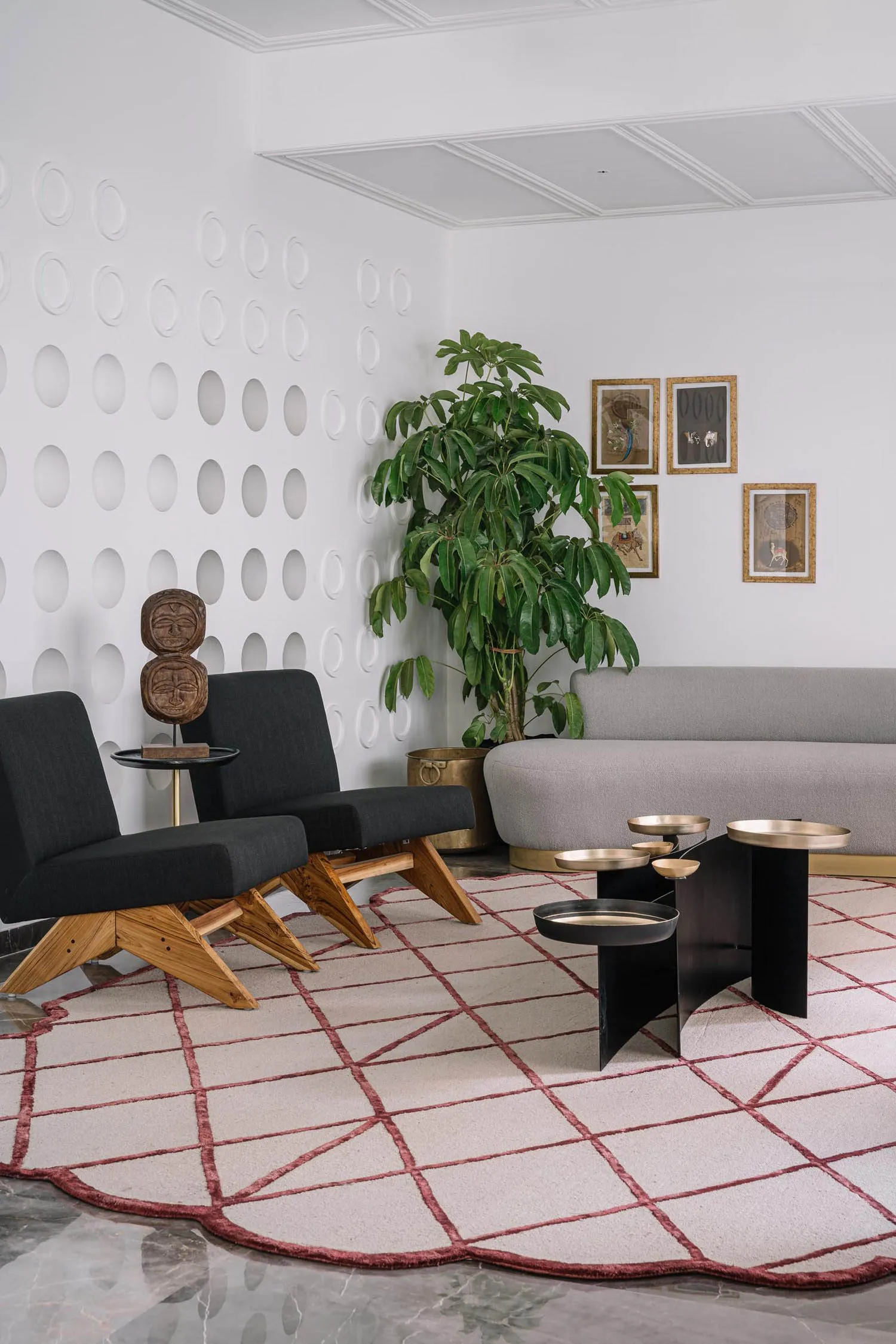 Photograph of a modern living room with a minimalistic design featuring a grey sofa, black chairs, a unique coffee table, and