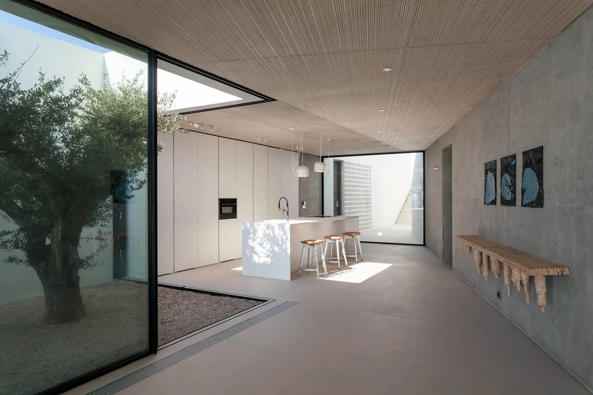 Modern residential interior featuring sleek, minimalist design with concrete flooring, glass walls, and a central kitchen isl