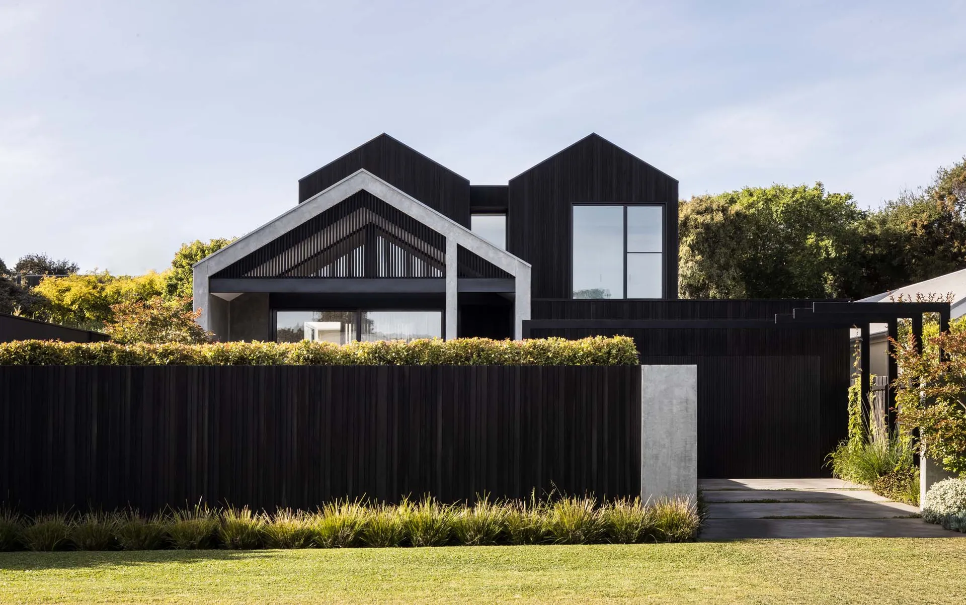 Modern black wooden exterior house with a fence and garden hidden behind it.