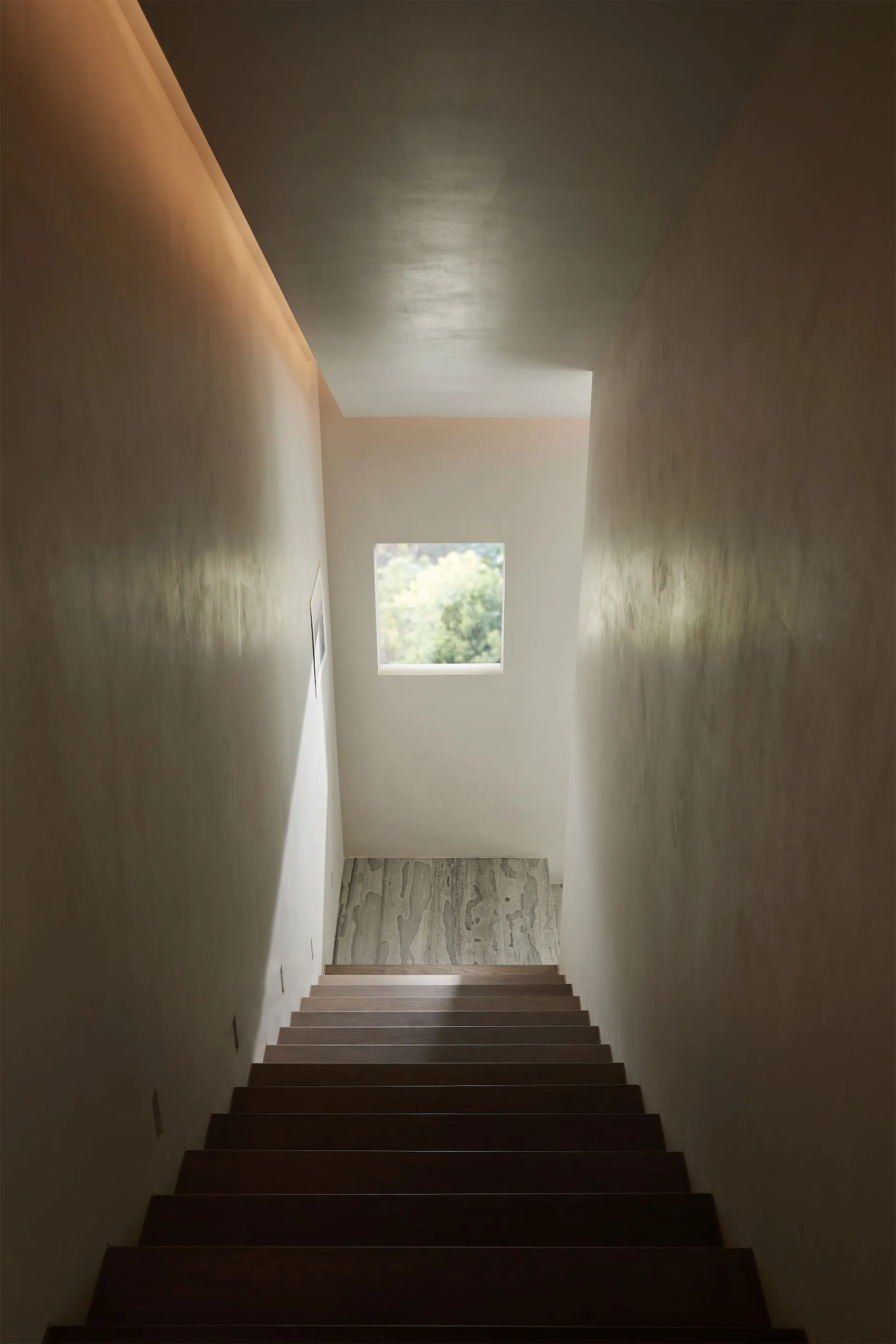 Modern indoor staircase with wooden steps, warm lighting, and a small rectangular window at the top.