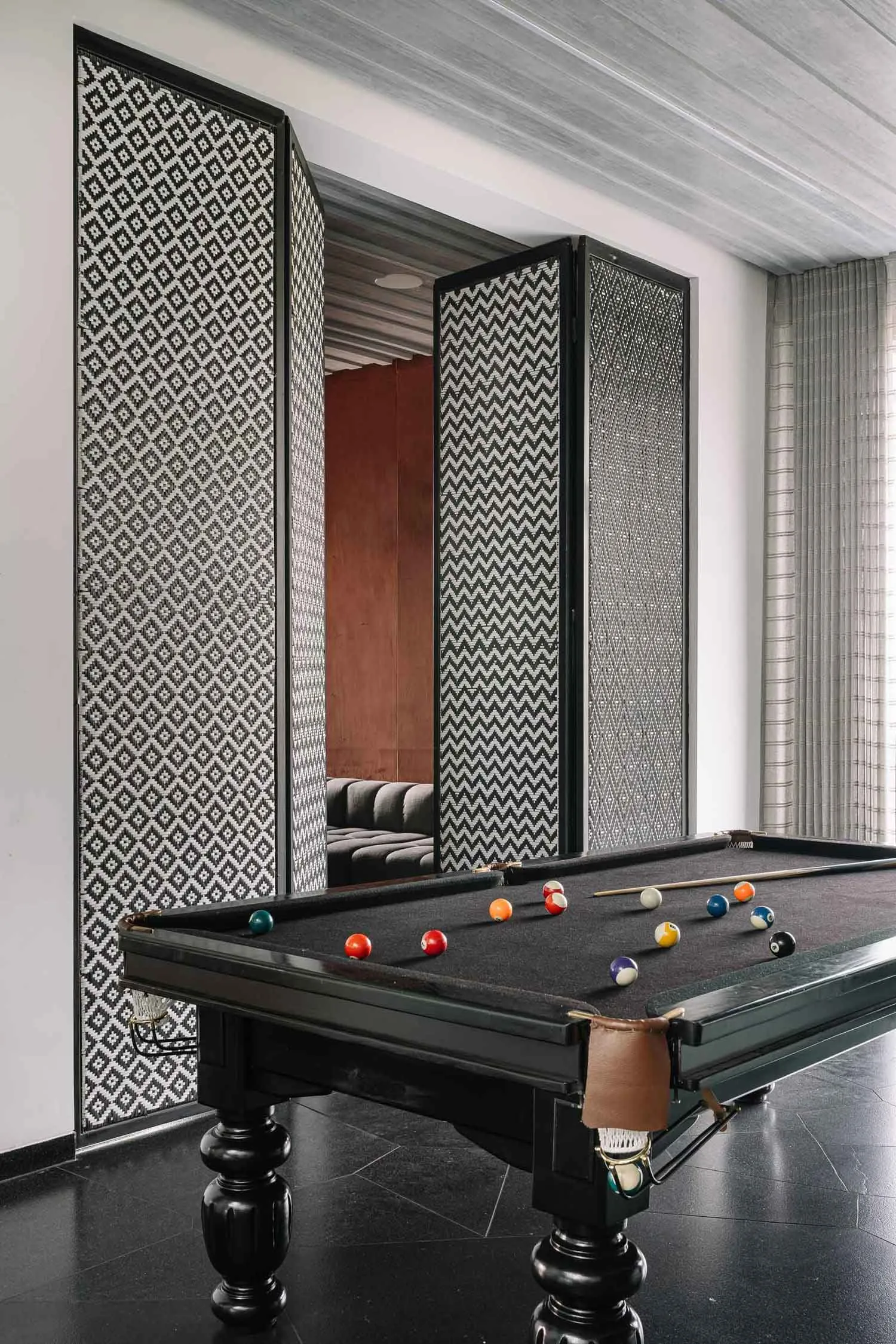 An industrial-style pool room with a black concrete floor, a pool table with billiard balls, and decorative floor-to-ceiling
