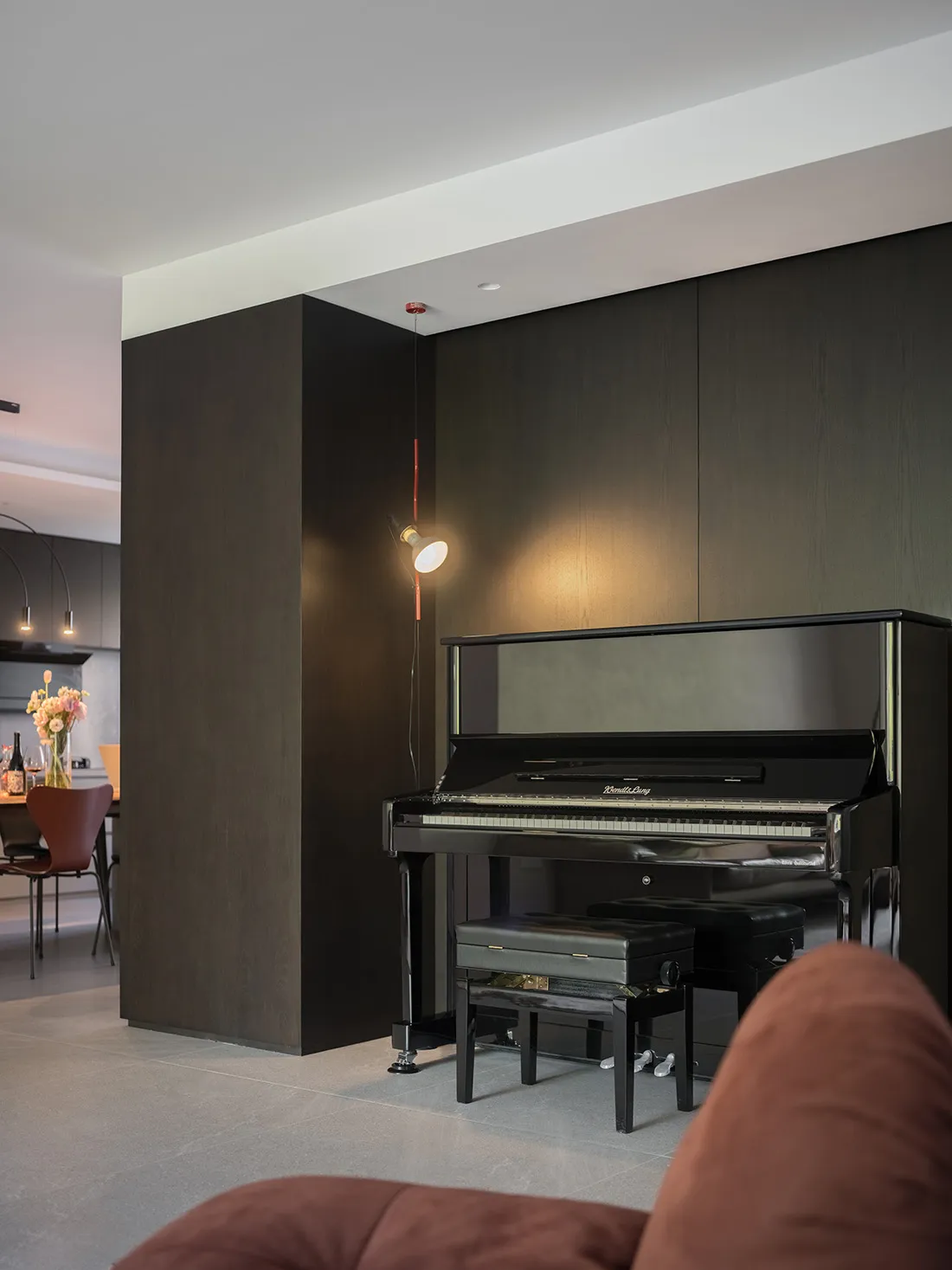 A minimalist living room featuring a piano corner with wooden cabinets and a brown sofa.