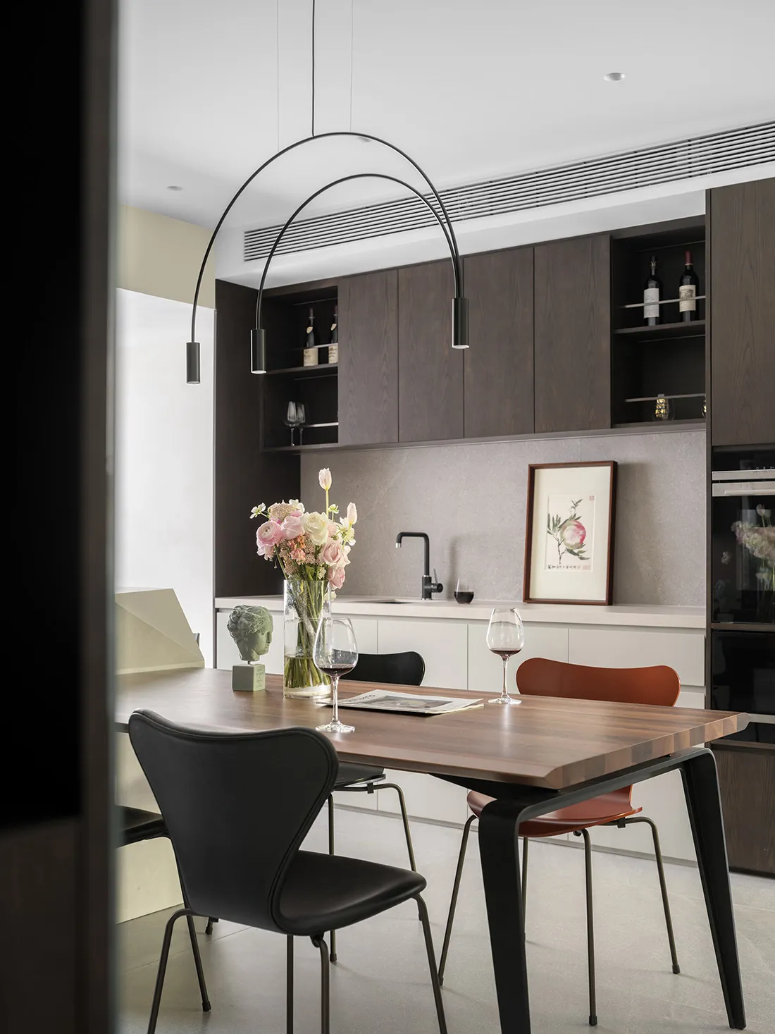 A modern residential kitchen with wooden cabinets, a dining table, and a vase of flowers.