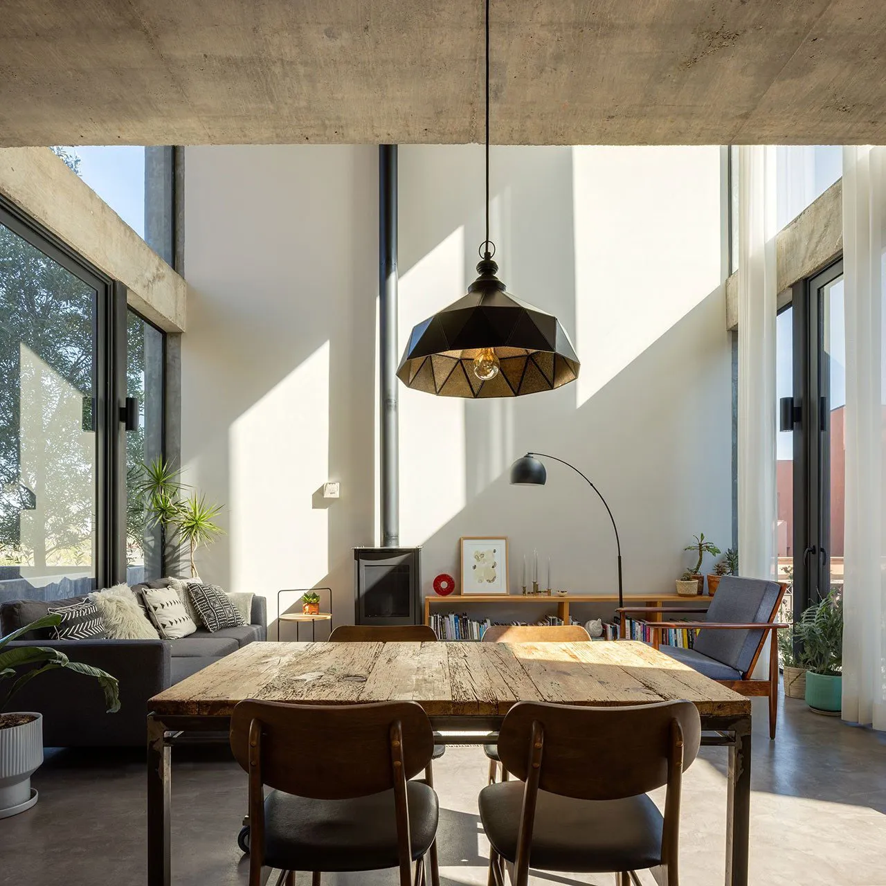 A spacious, modern living and dining area featuring exposed concrete beams, wooden dining table, and contemporary decor.