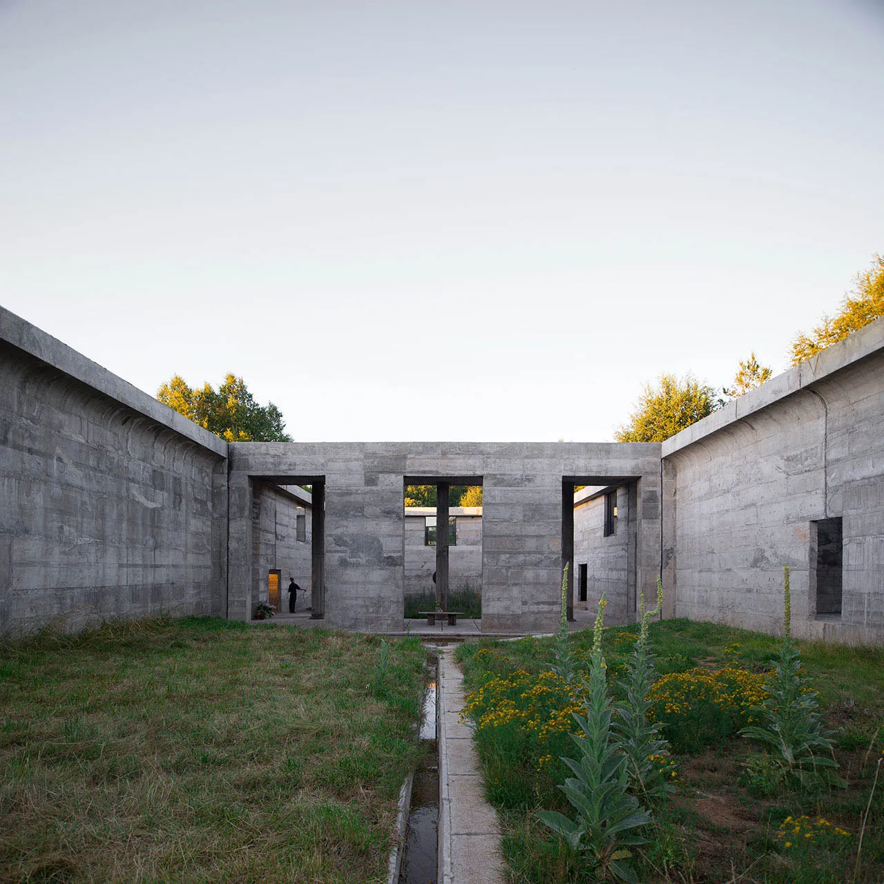 一座極簡混凝土結構,擁有大型開口,路徑穿過花園。