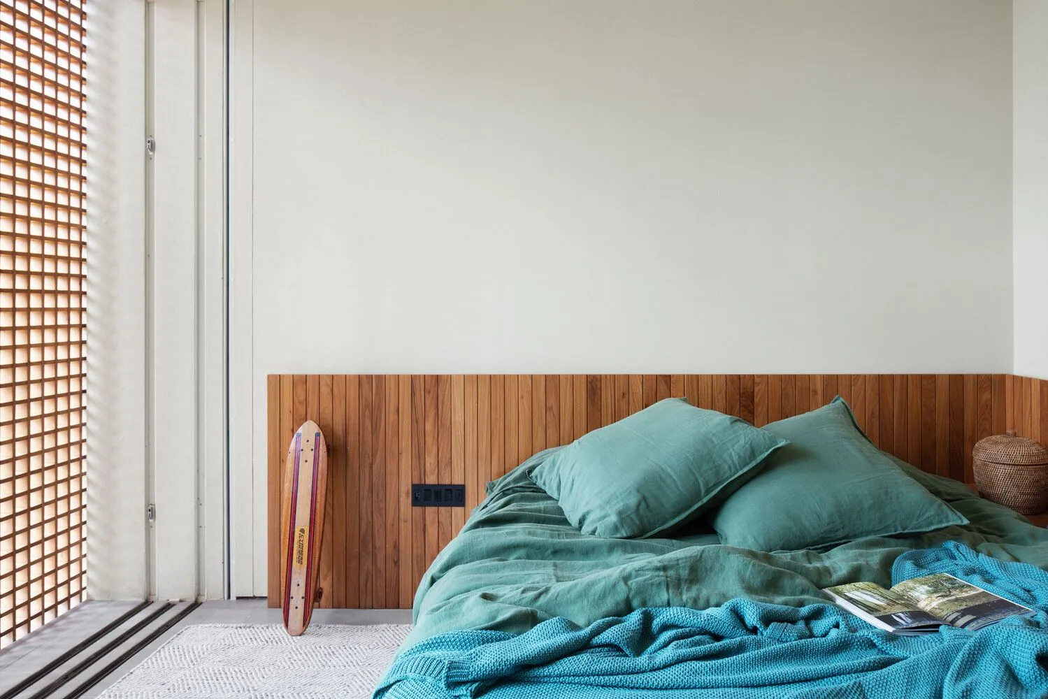 Minimalist bedroom featuring teal bed linens and a wooden headboard.