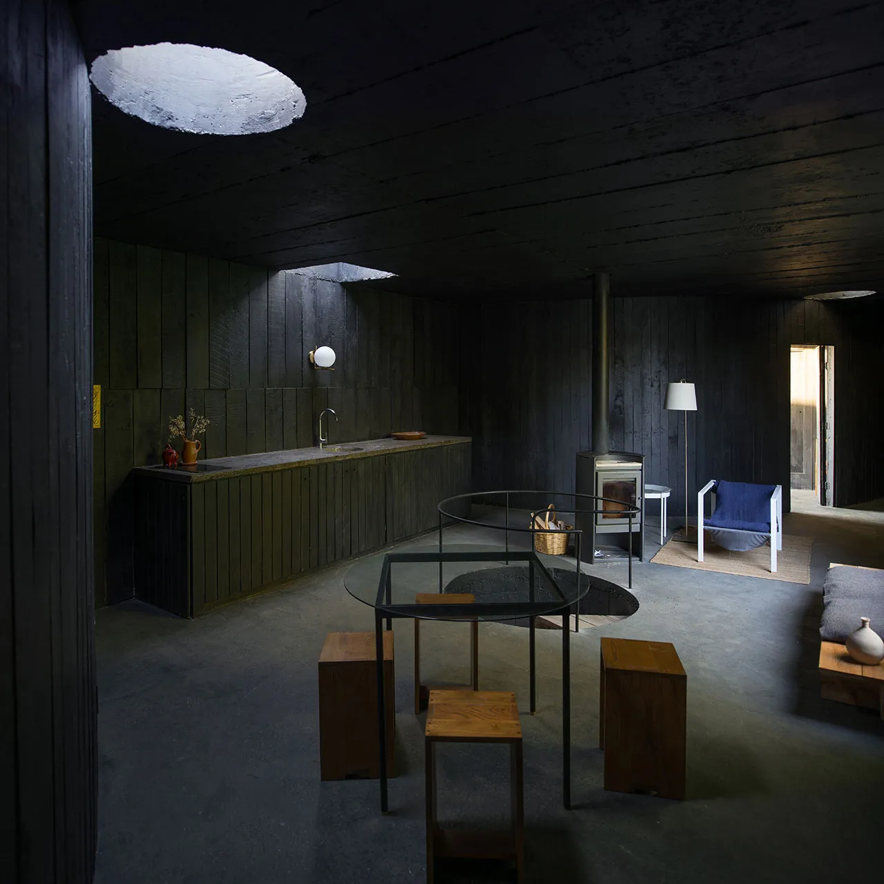 A minimalist kitchen with a concrete floor, walls, and table, and wooden stools.