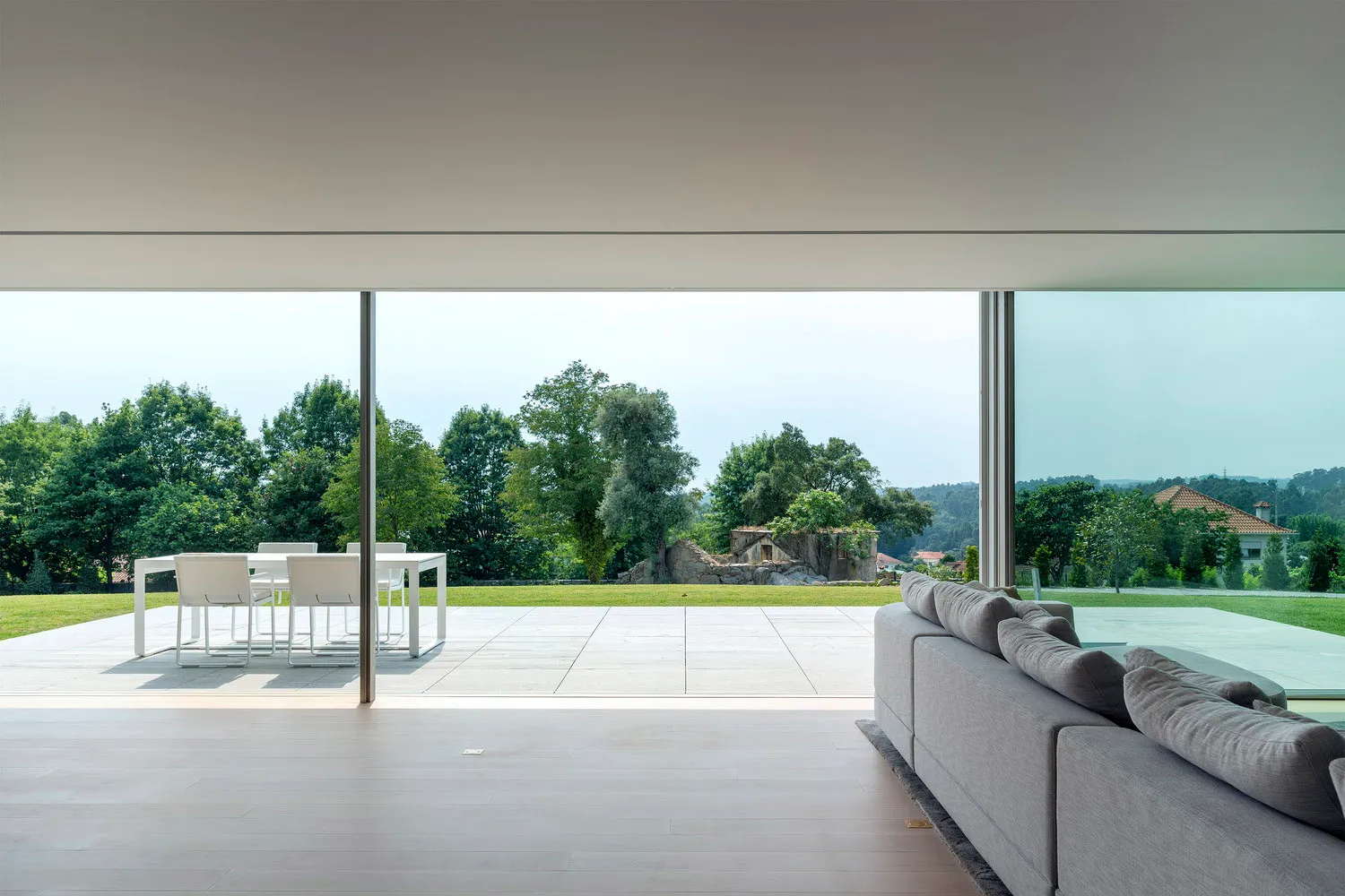 Modern minimalist living room with a large glass wall overlooking a lush green landscape.