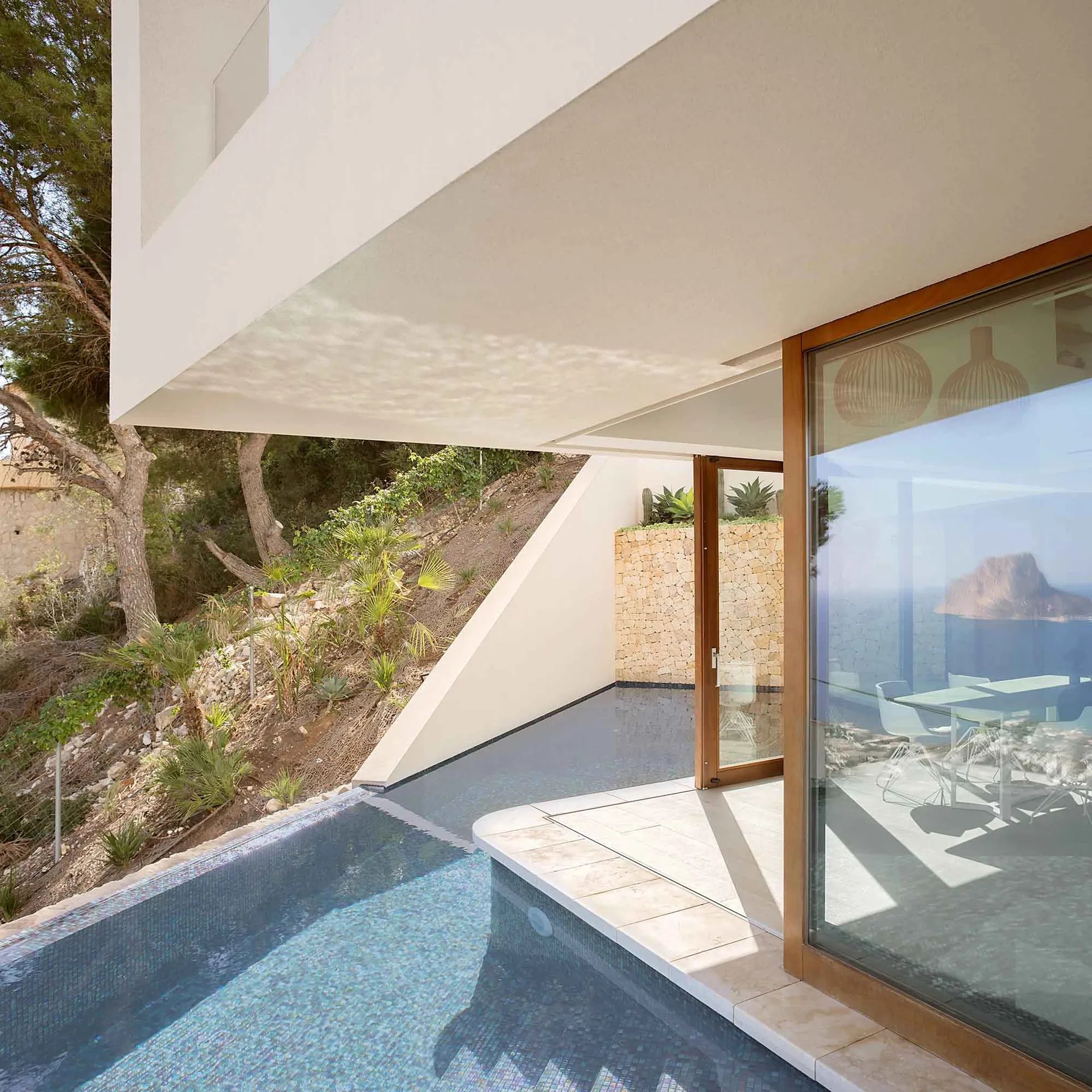 Modern minimalist poolside patio with concrete flooring and outdoor furniture overlooking natural landscape