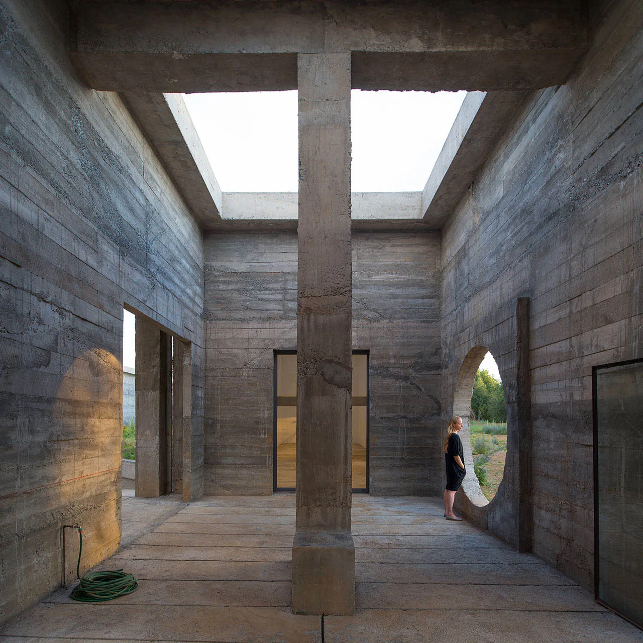 A minimalist concrete interior space with skylights and a woman standing in front of an archway.
