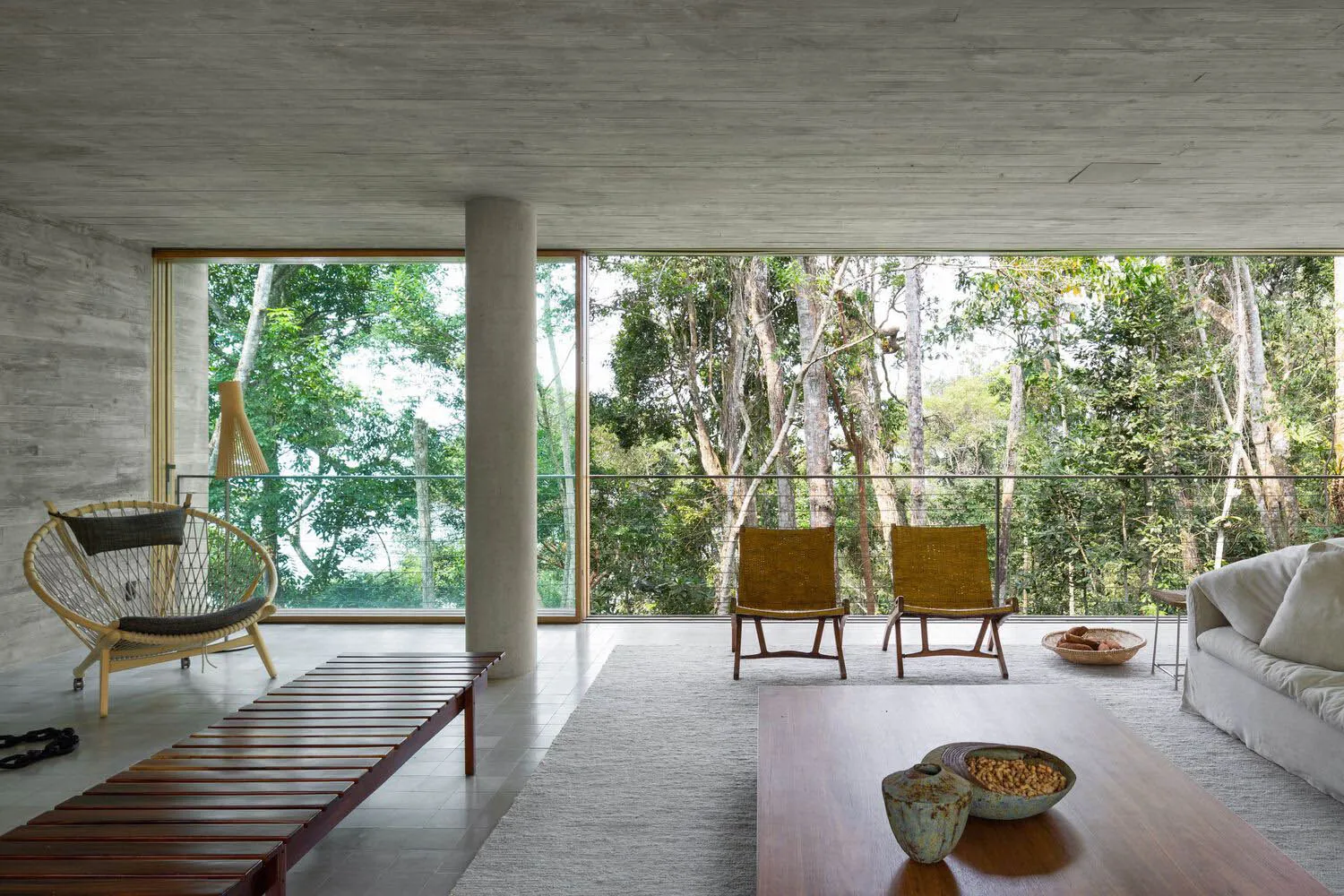 Modern living room with concrete walls and large windows overlooking a forest.