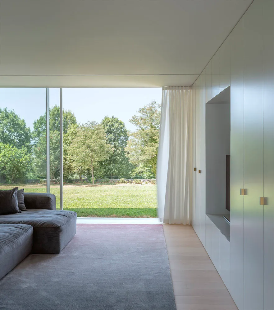 Modern minimalist living room featuring a glass wall, concrete floor, and fabric furniture.