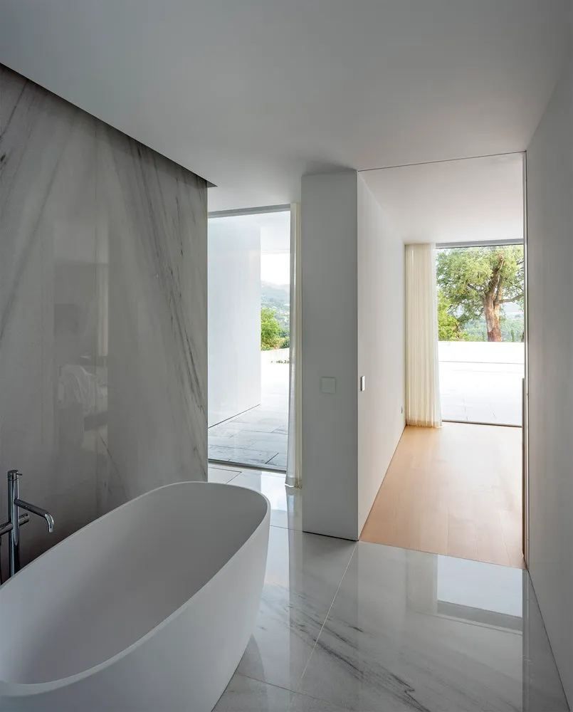 Modern minimalist bathroom with white marble finishes and glass enclosure.