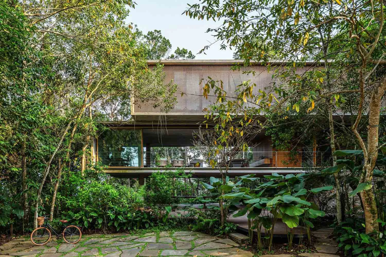 Modern house exterior featuring wooden panels and large windows, surrounded by lush greenery.