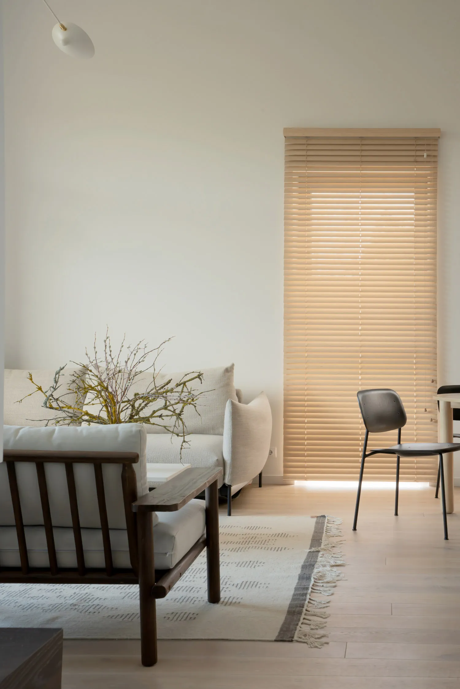 Minimalist living room with wooden flooring, white walls, and a window with wooden blinds, showcasing budget-friendly design